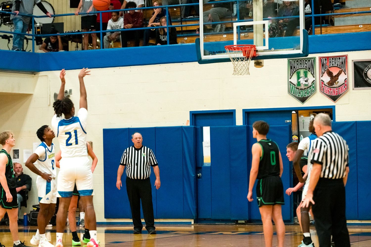 A high school basketball player in blue shoots a free throw while referees and players watch near the lane.