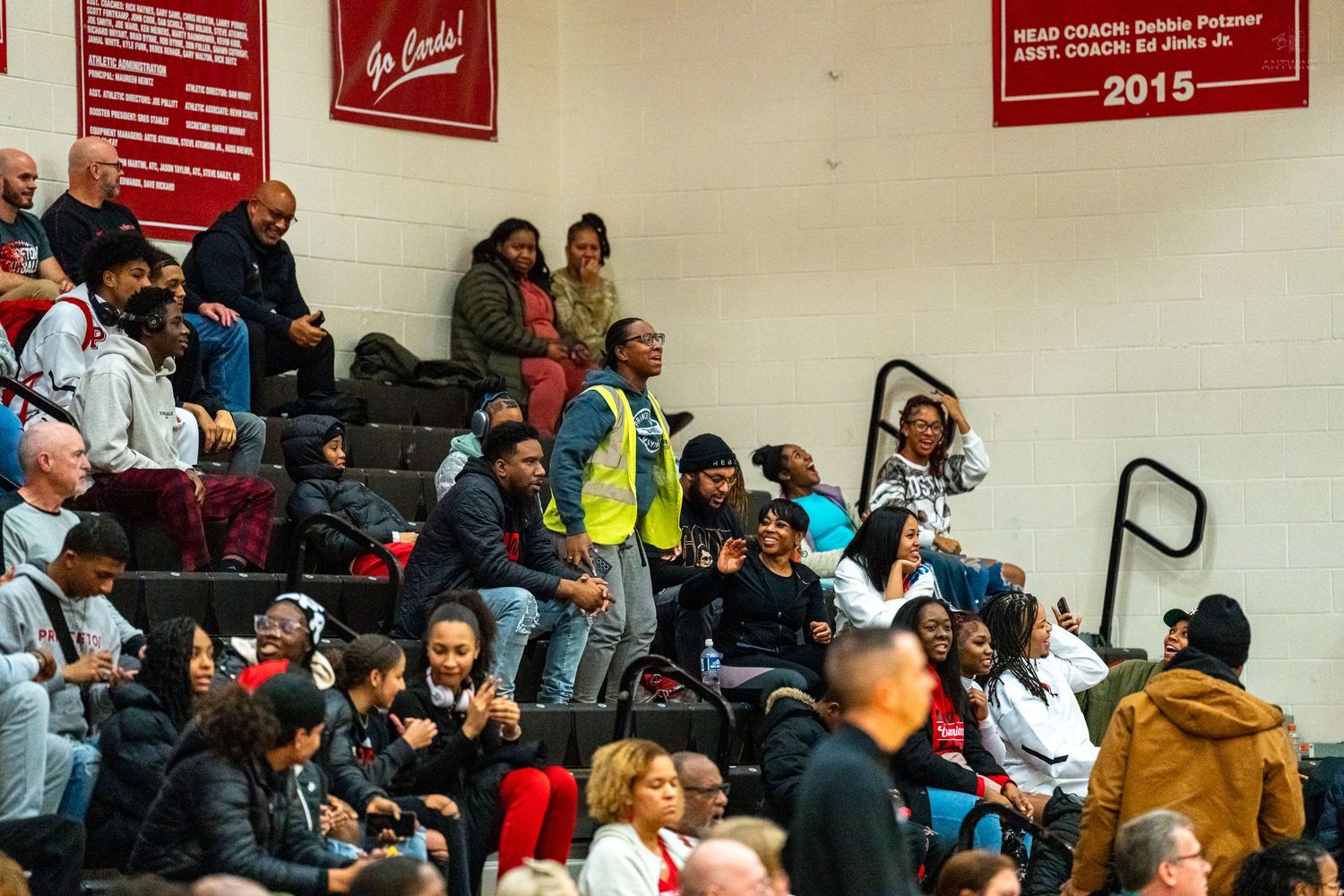 Diverse crowd of fans watches high school basketball game from bleachers in packed gymnasium.