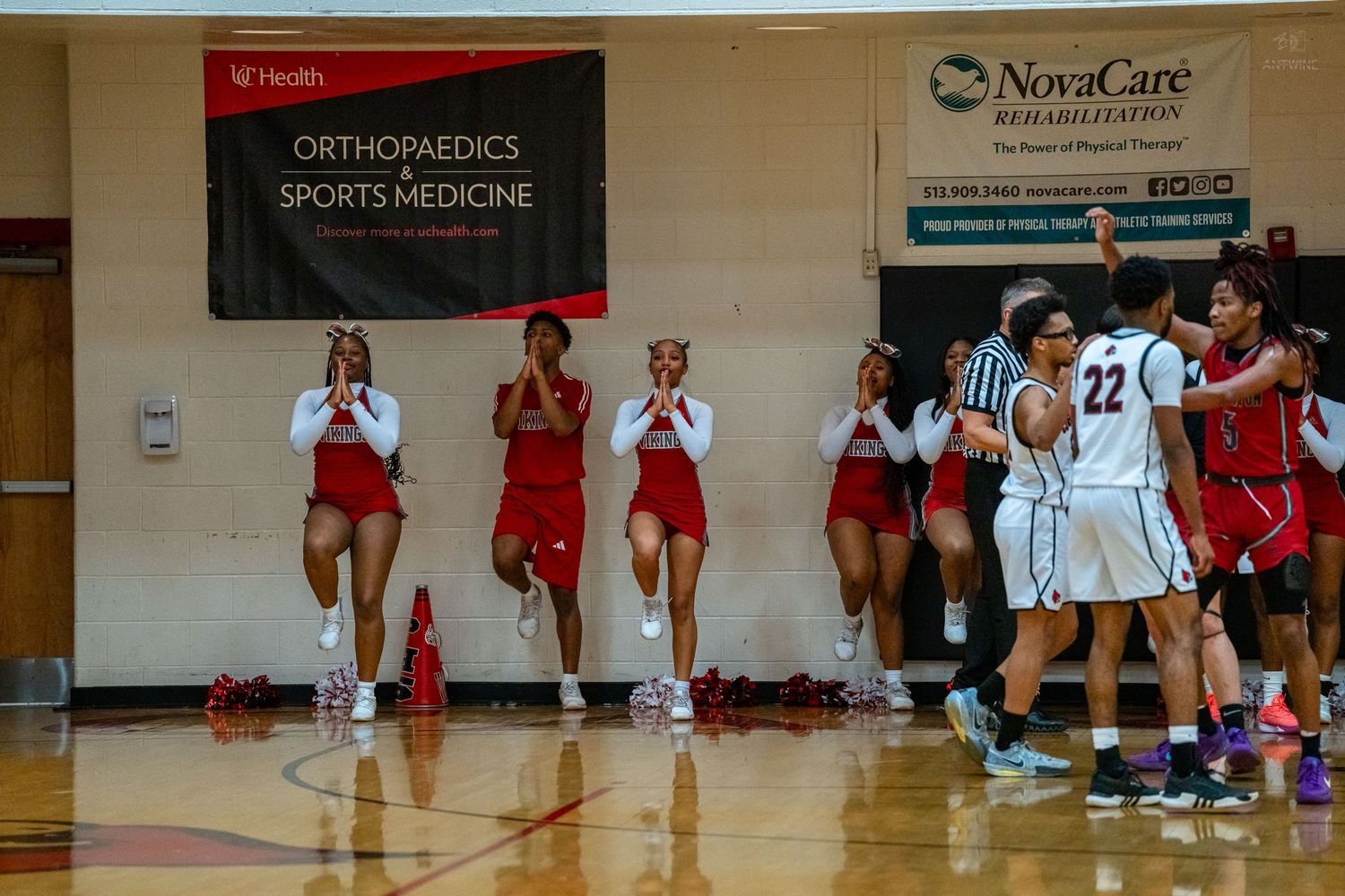 Cheerleaders and players near sideline during high school basketball game under Orthopaedics Sports Medicine banner.