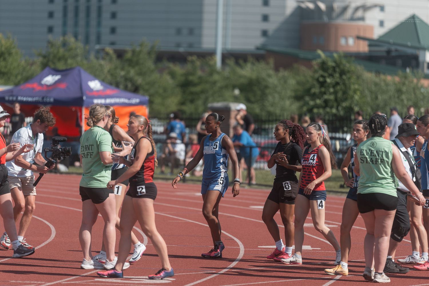 Track and field athletes exchange handshakes and congratulations on the red track after a relay race competition.