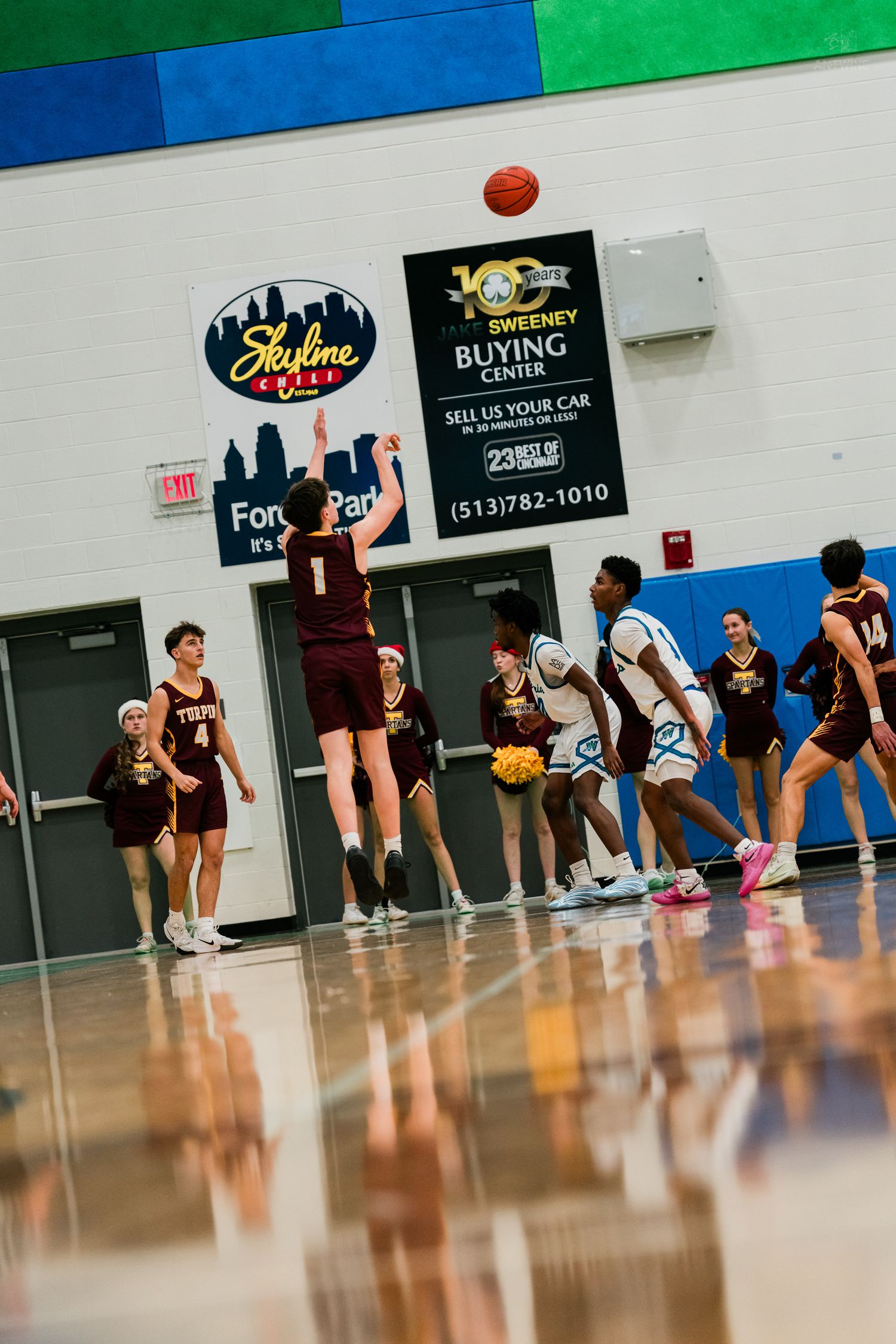 Player #1 in maroon shoots a free throw during a high school basketball game in a gym with sponsor banners.