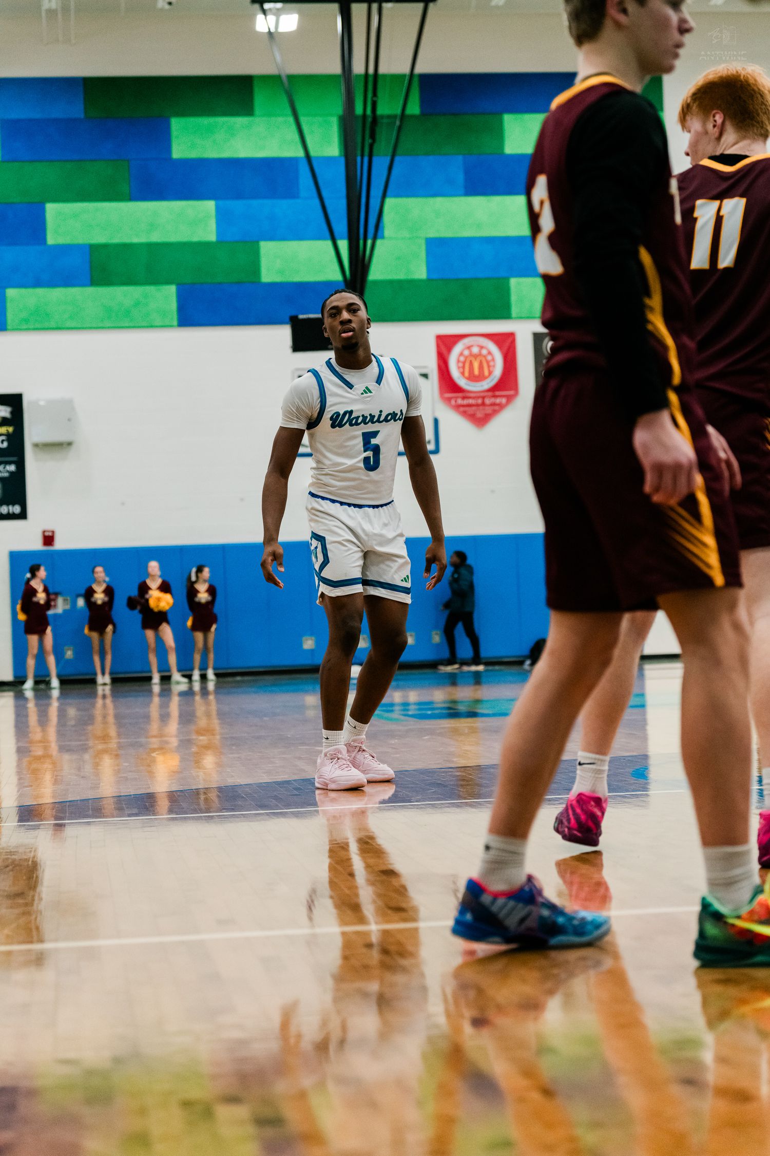 Warriors player #5 in white uniform stands on the court during a high school basketball game.