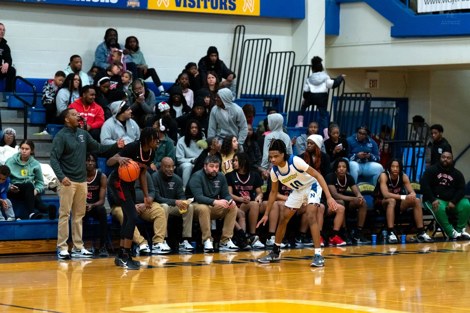 High school basketball player number 10 dribbles along the sideline in front of the team bench.