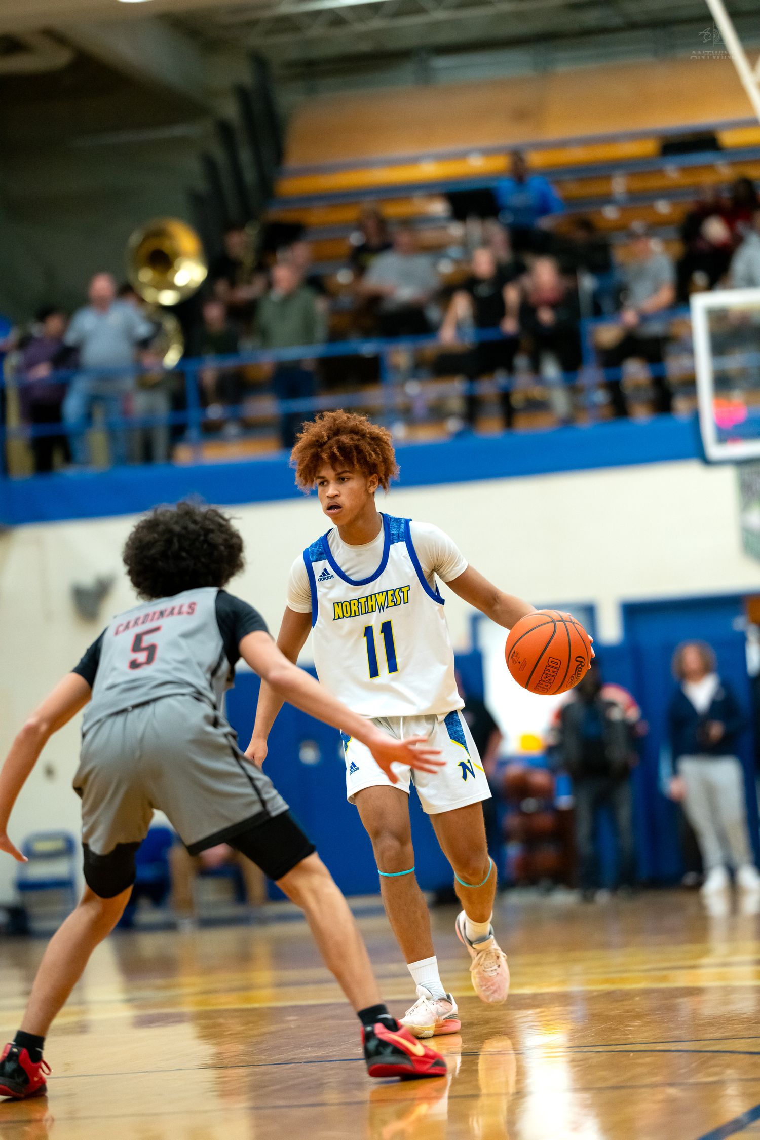 Player #11 in white dribbles basketball against defender #5 in gray during high school game.