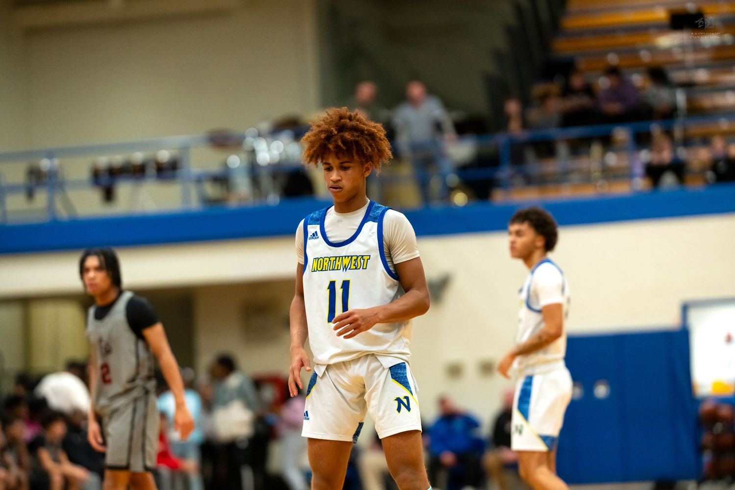 Player #11 in Warriors uniform walks on court during high school basketball game in blue gymnasium.