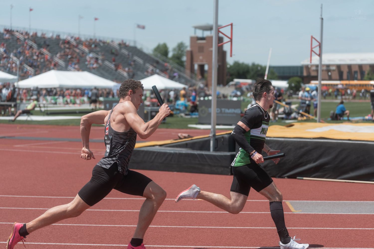 Two male sprinters compete in a track race at a packed outdoor stadium during a high school state championship meet.