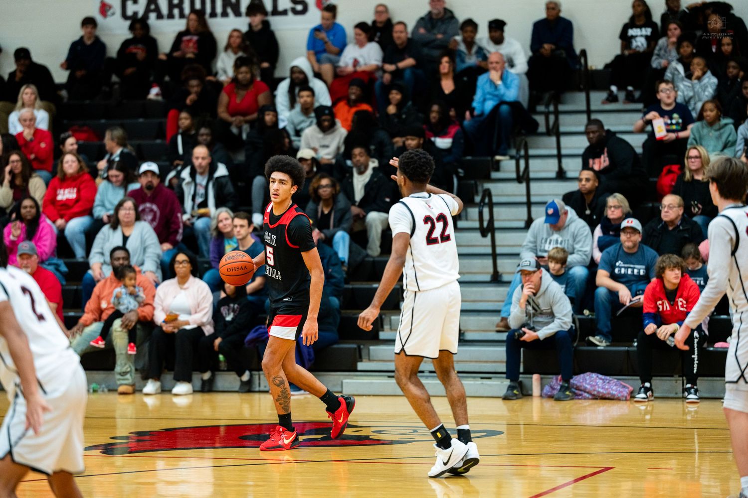High school basketball player dribbles ball while defender guards during Cardinals home game.