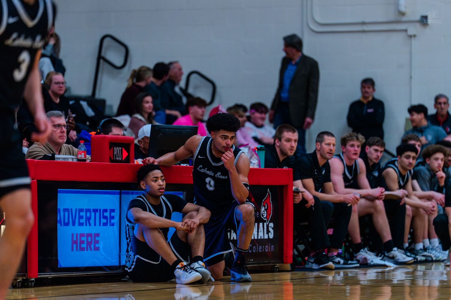 High school basketball players watch from the bench during a competitive game.