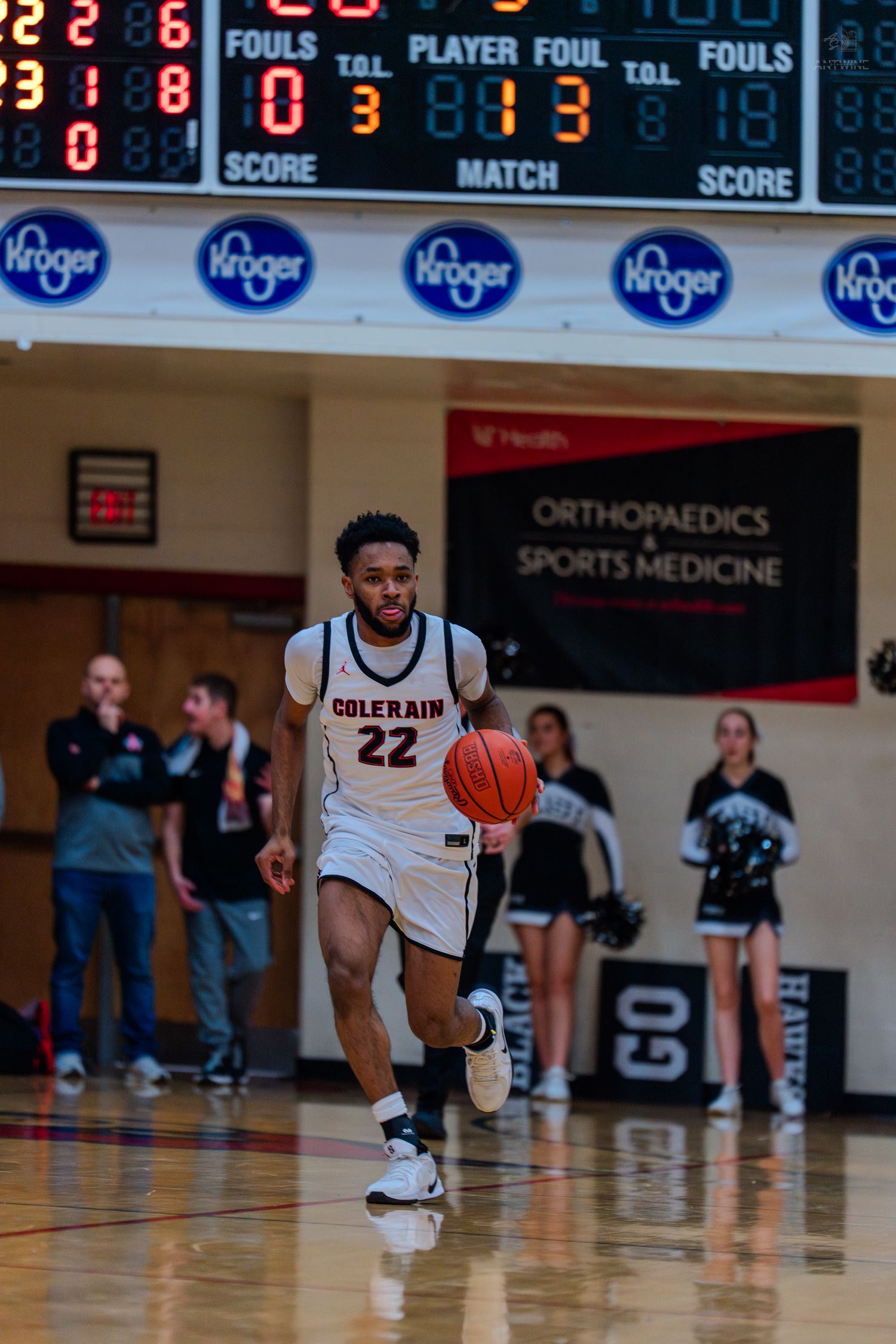 Colerain #22 basketball player dribbles upcourt during a high school game with scoreboard visible.