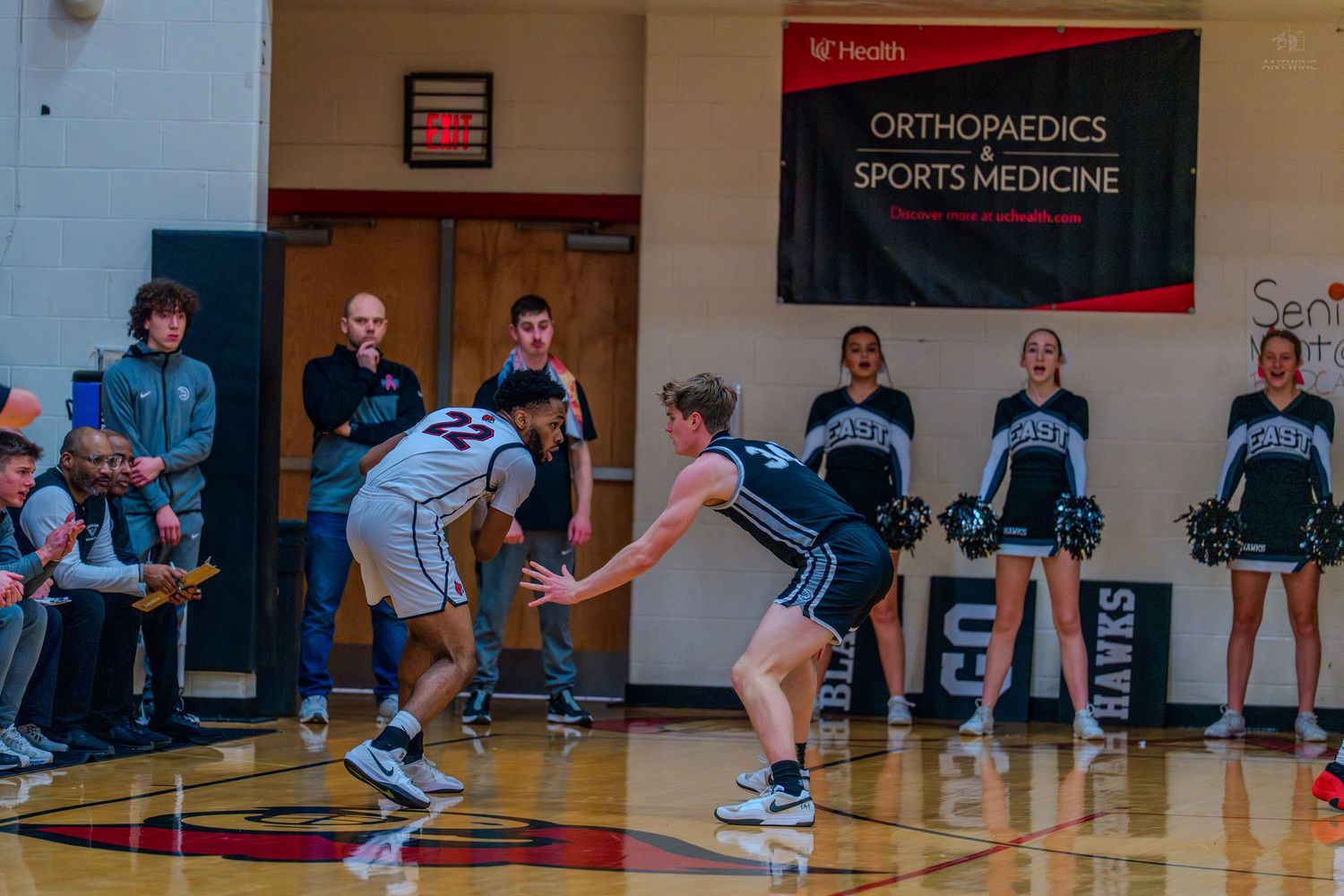 Male high school basketball player defends opponent near the sideline during a game.