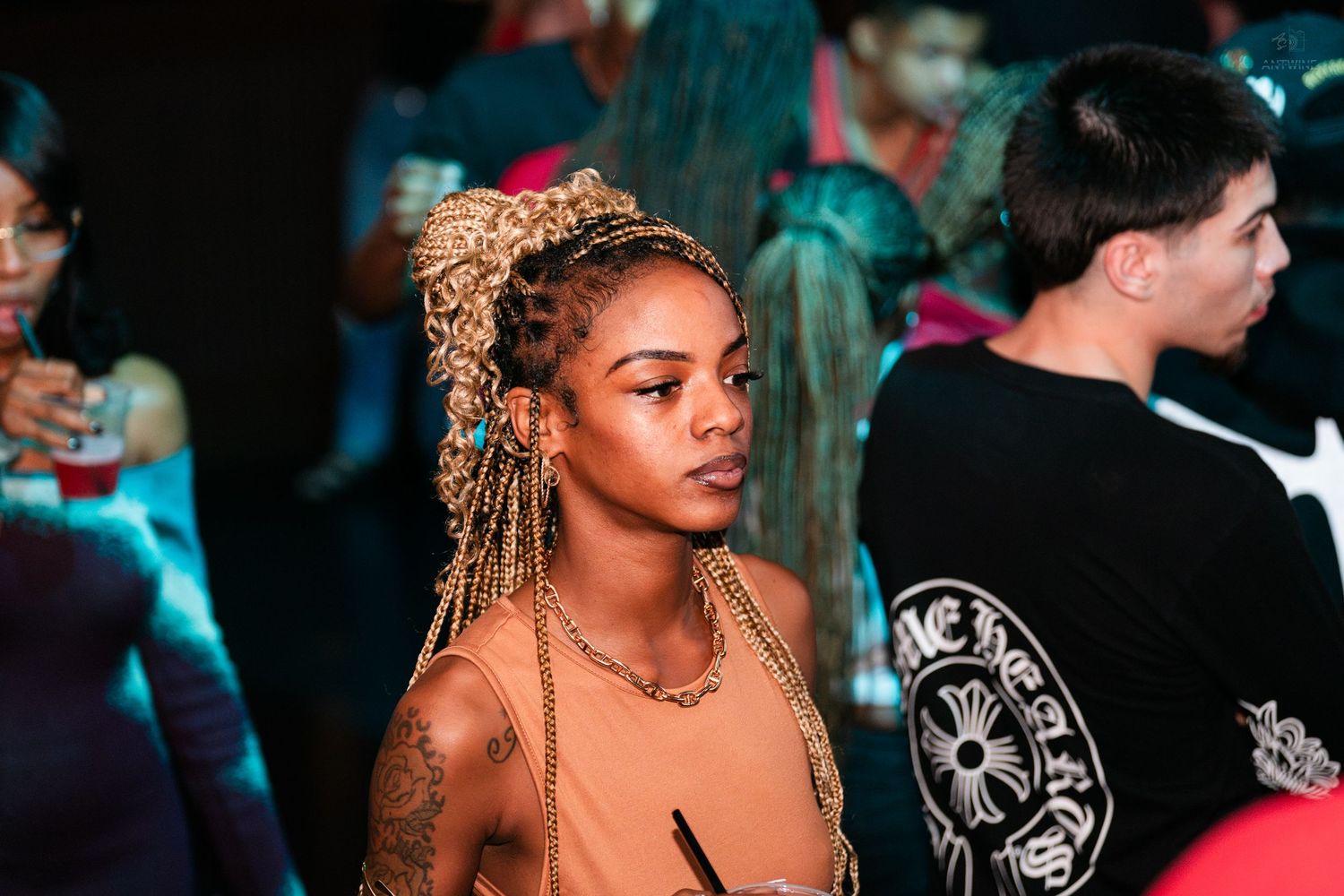 Woman with decorative braids standing in a crowded nightclub environment.