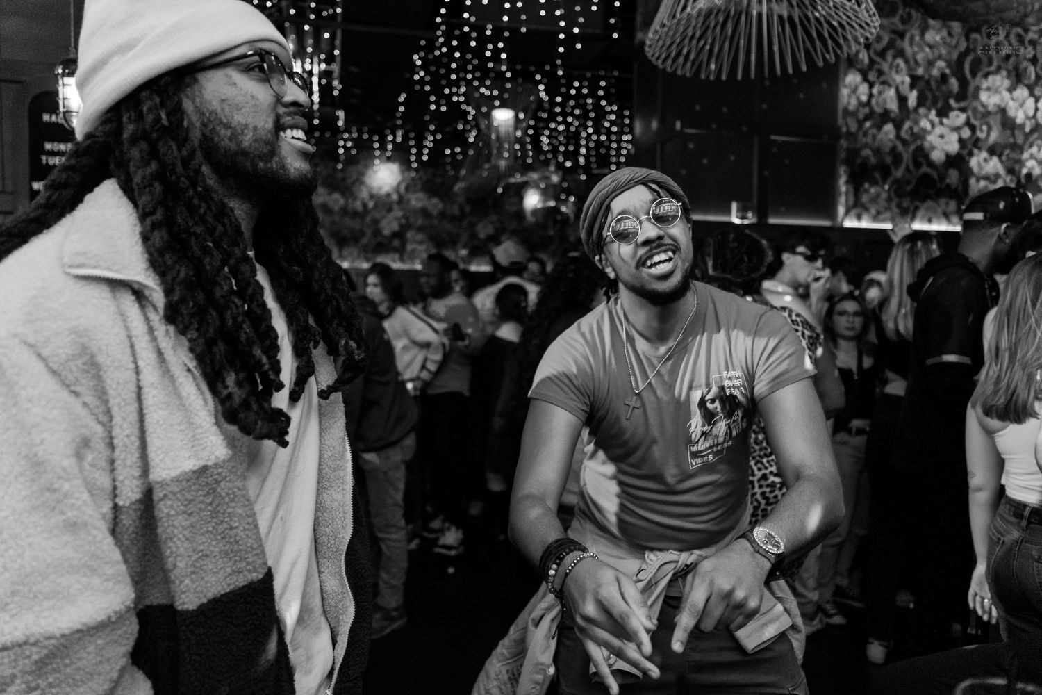 Two men laughing together at a crowded nightclub event, captured in candid black and white photography.