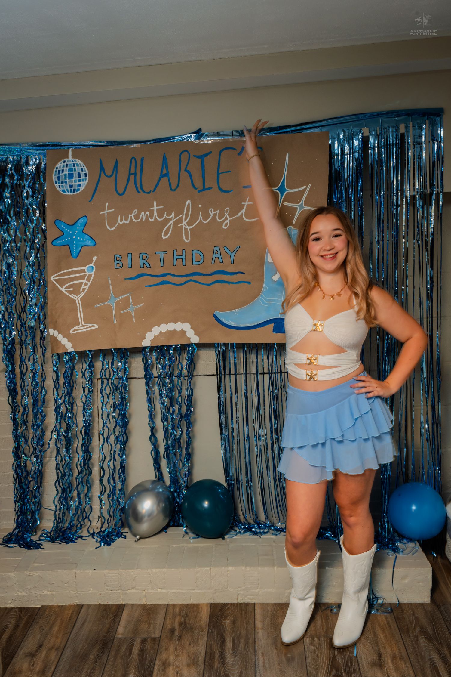 Woman celebrating 21st birthday posing by handmade cardboard sign with blue tinsel backdrop.