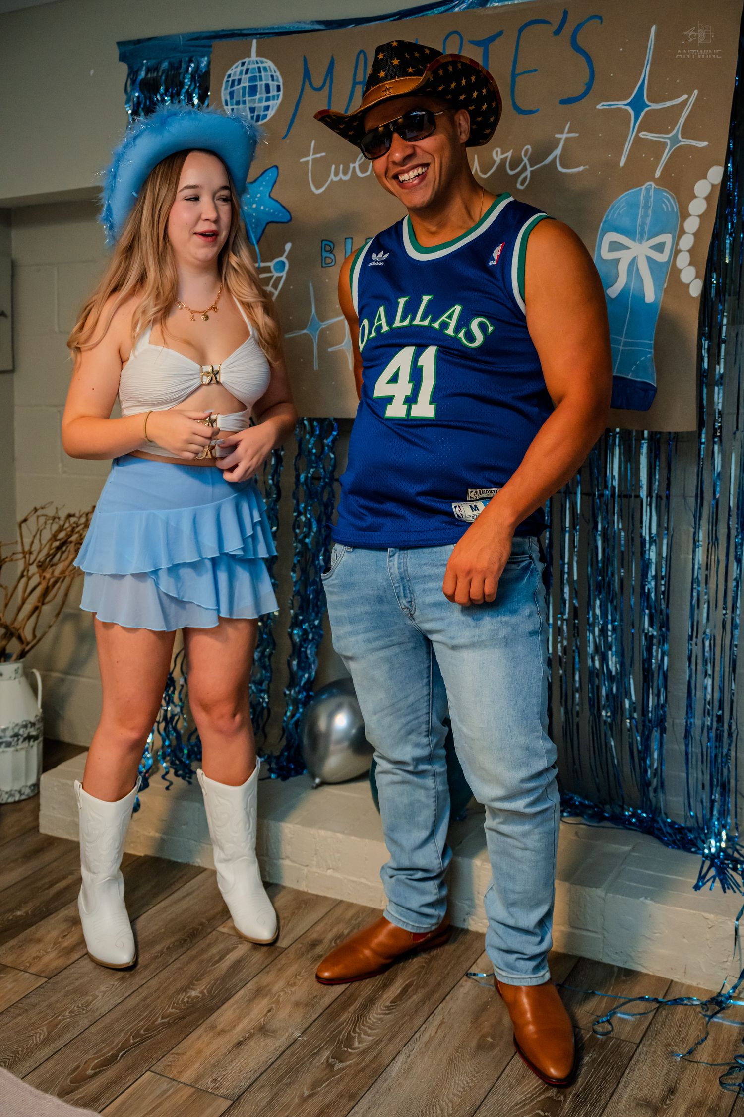Couple smiling in coordinated blue outfits at a Dallas Mavericks themed birthday celebration.