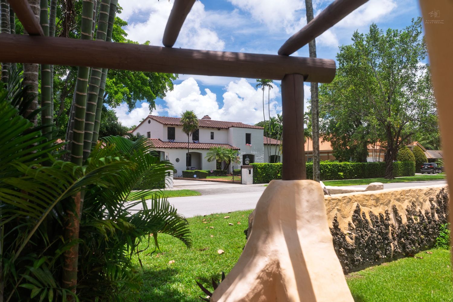 A white Spanish-style house viewed through tropical palm trees and green landscaping.