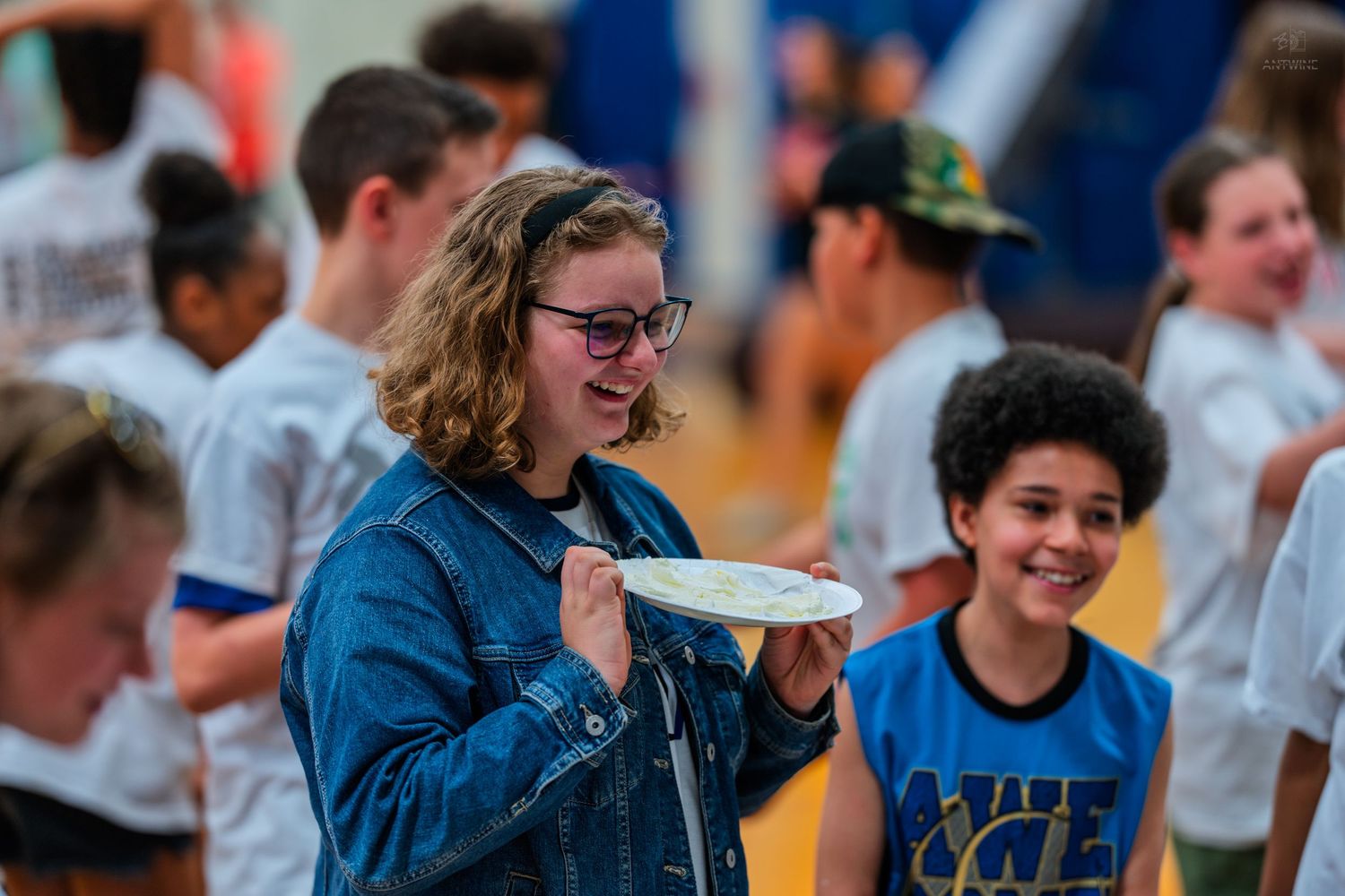 Students smile and hold a frisbee during an outdoor school event in a gymnasium setting.