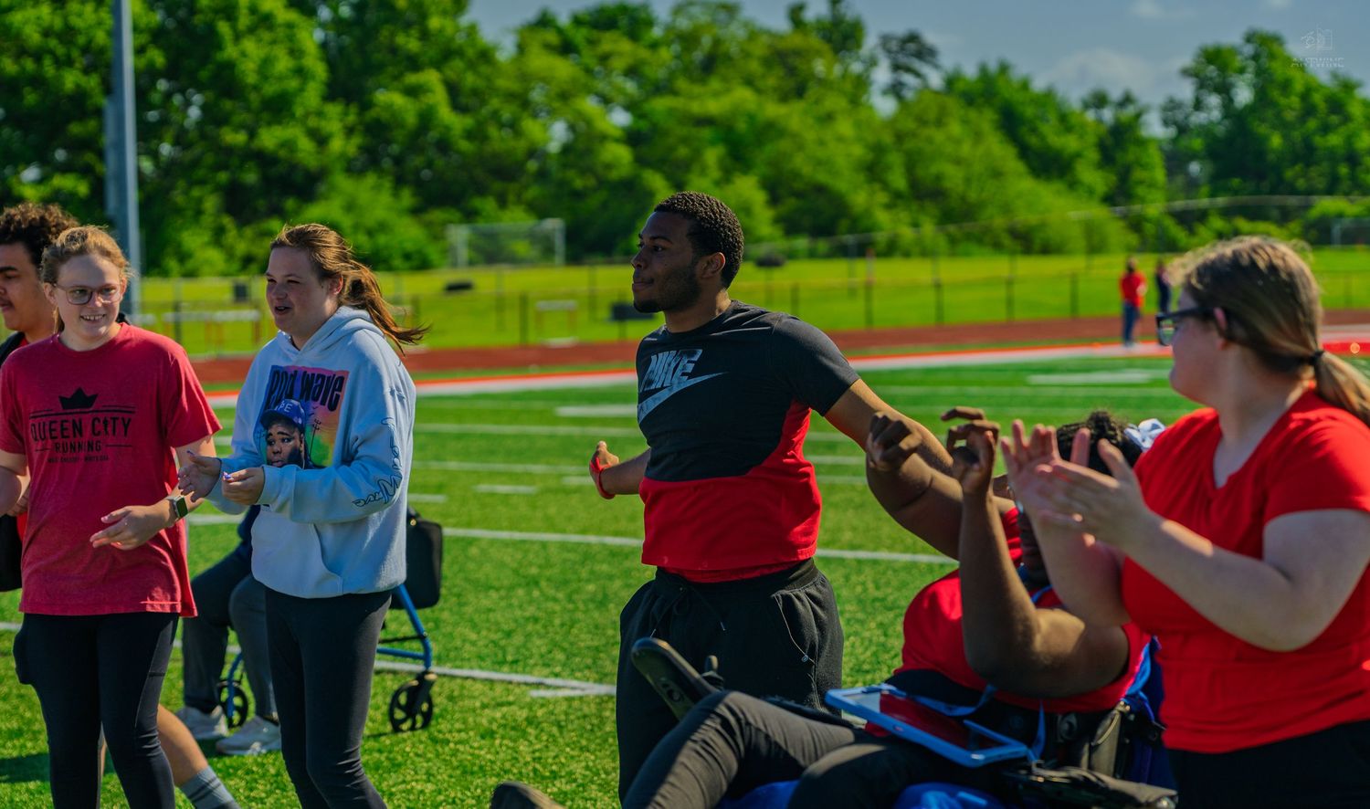Students participate in outdoor track and field activities on a green sports field on a sunny day.