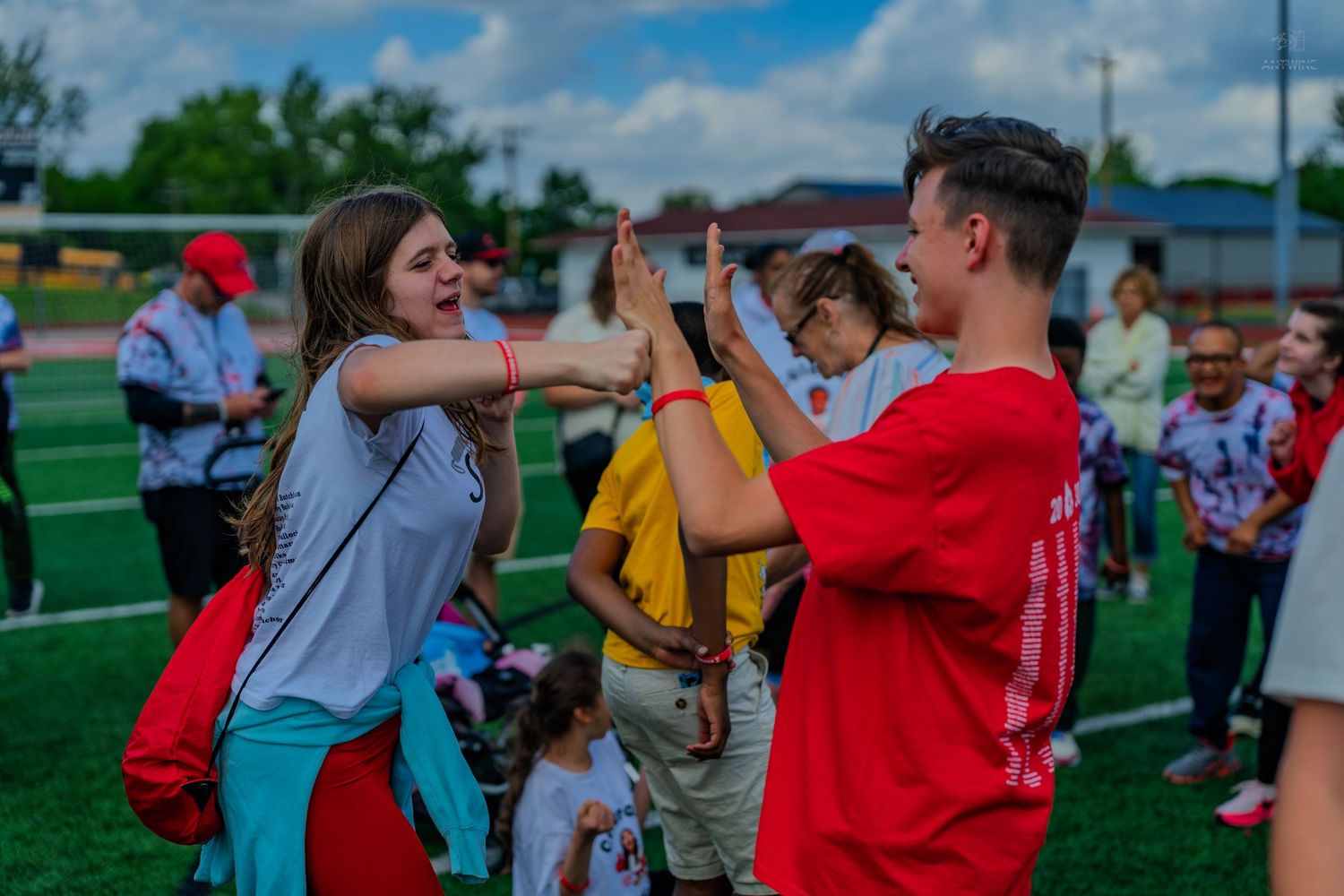 Two teens high-fiving on a sports field during an outdoor youth event on a cloudy day.