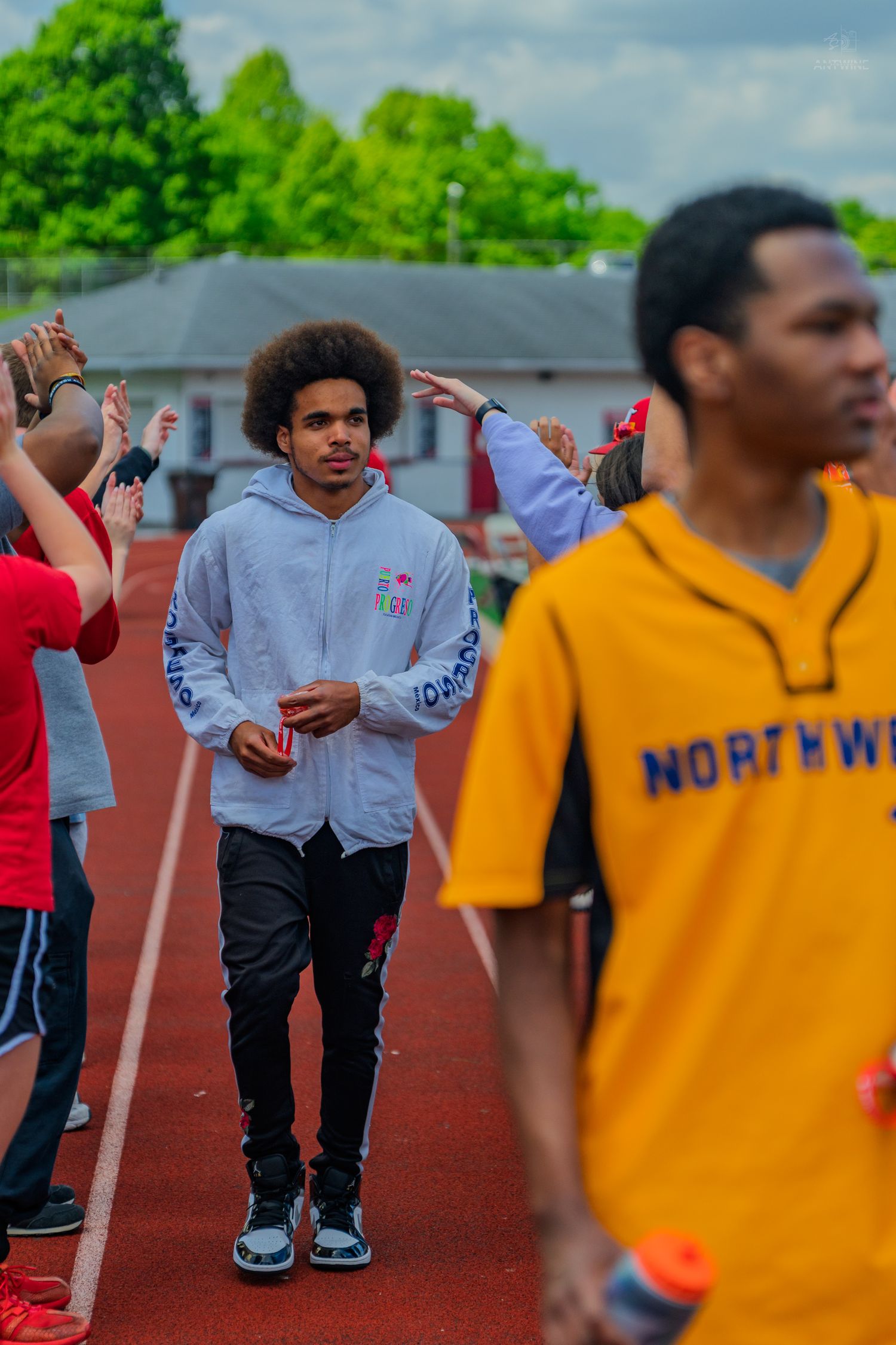 Young athletes on a red track, one in a gray hoodie and another in a yellow Northwest jersey, during a sports event.
