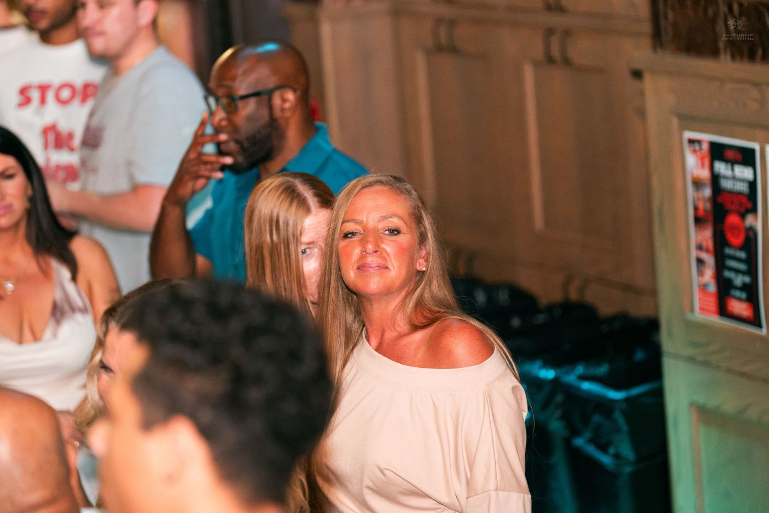 Woman in white off-shoulder top looking back at a crowded nightclub.