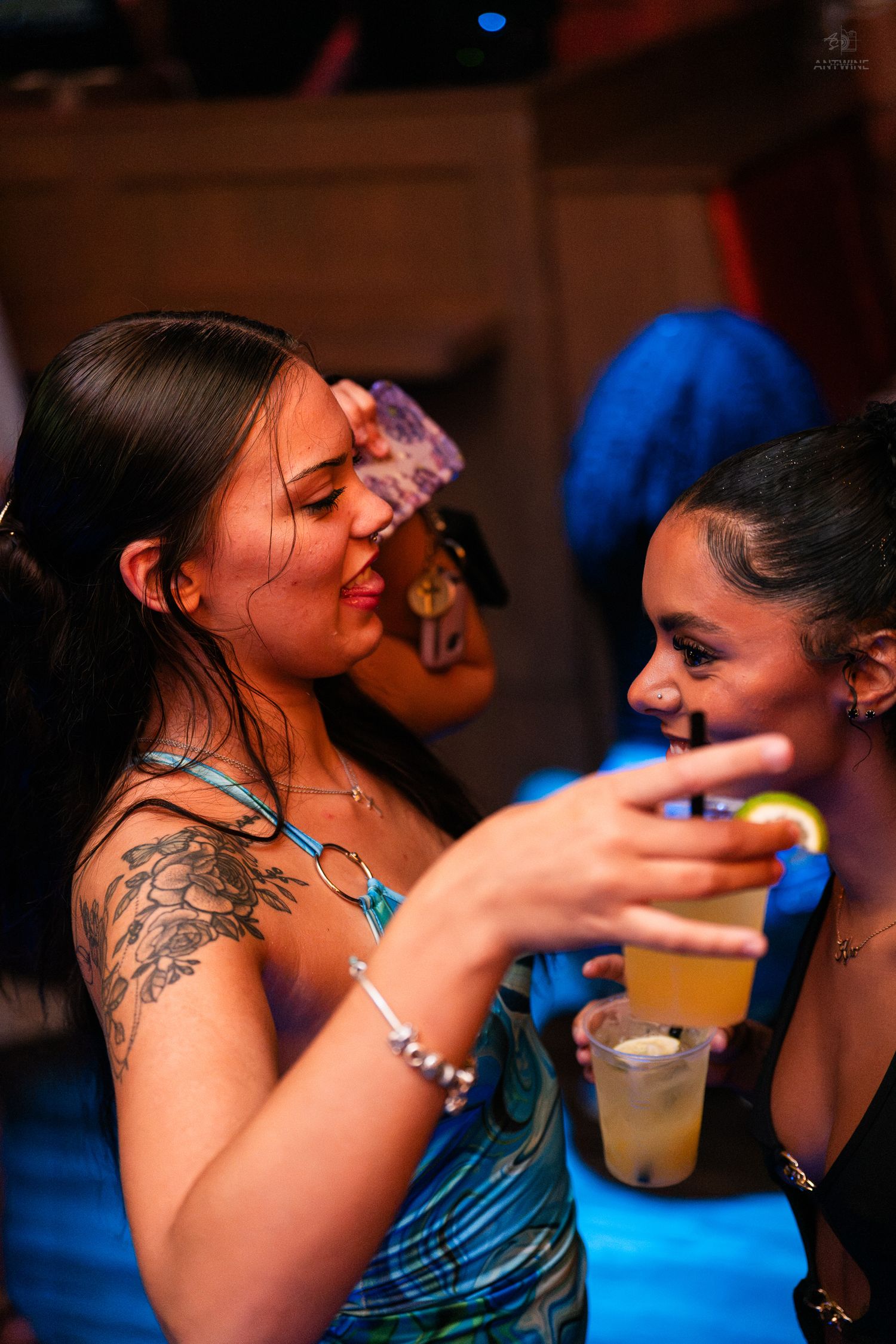 Two women sharing drinks and laughing together on a vibrant nightclub dance floor.