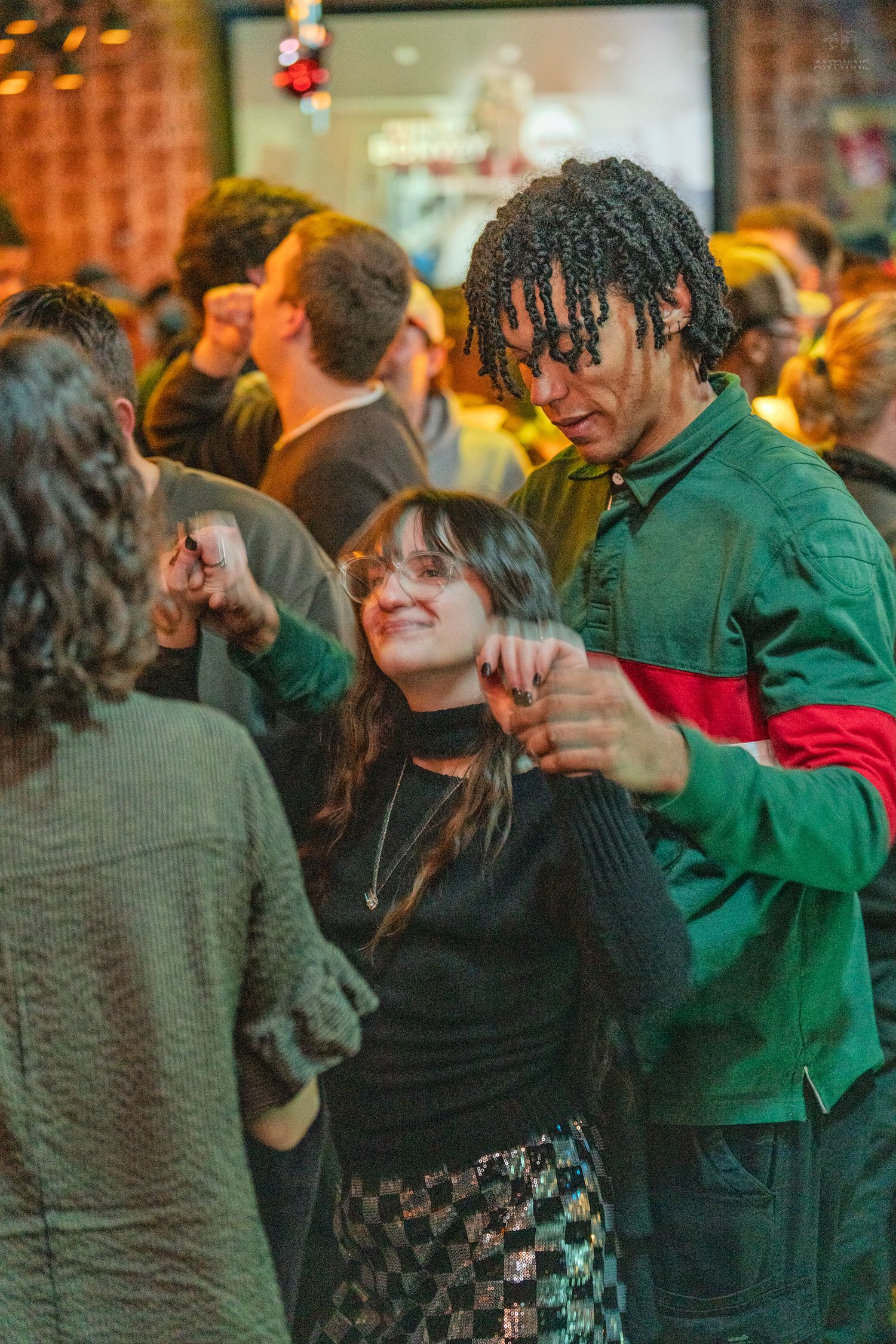 Man in green jacket and woman in black sweater dancing together at a lively party.