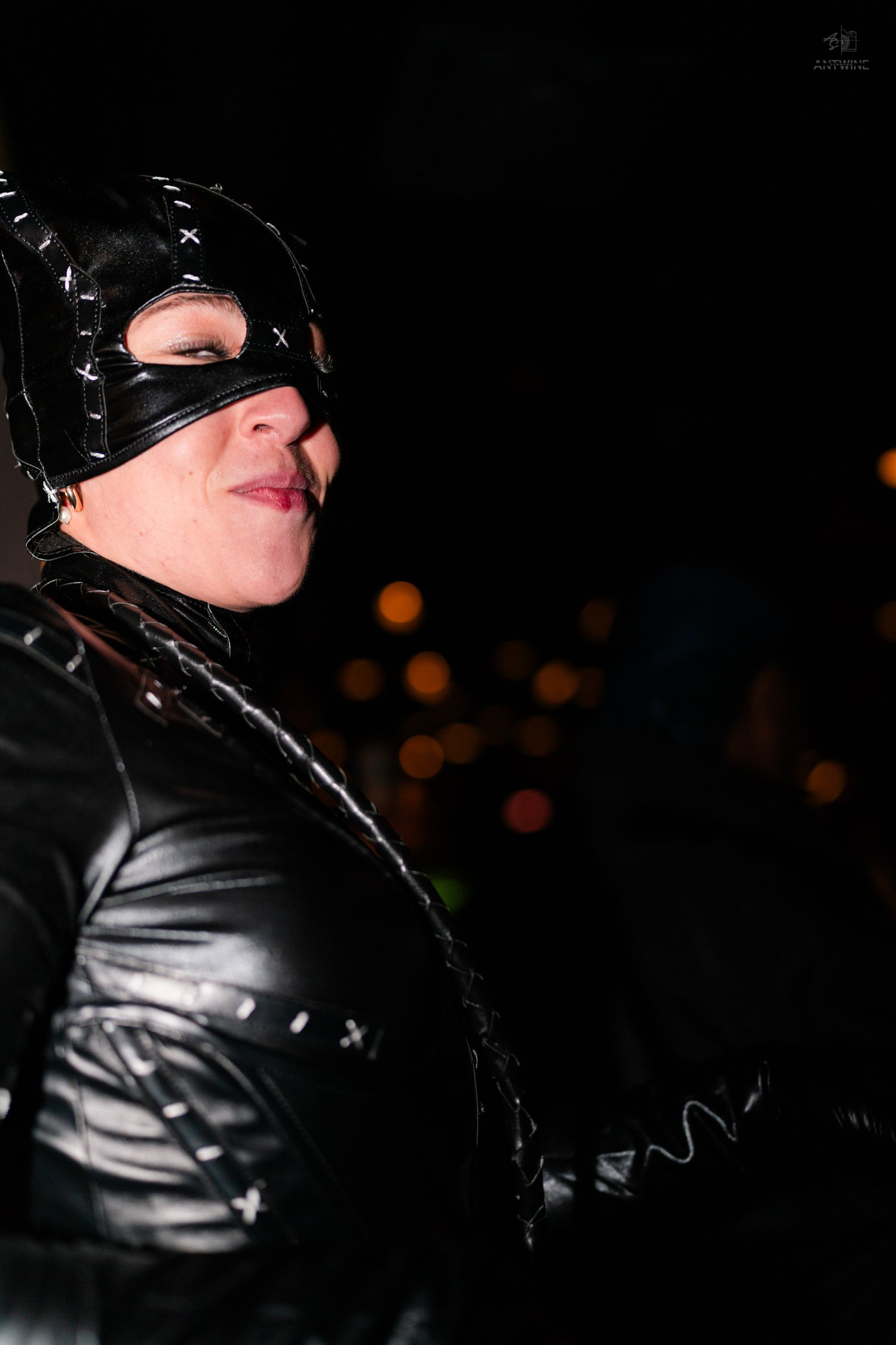 Woman in black Catwoman costume and mask poses at night with bokeh lights in background.