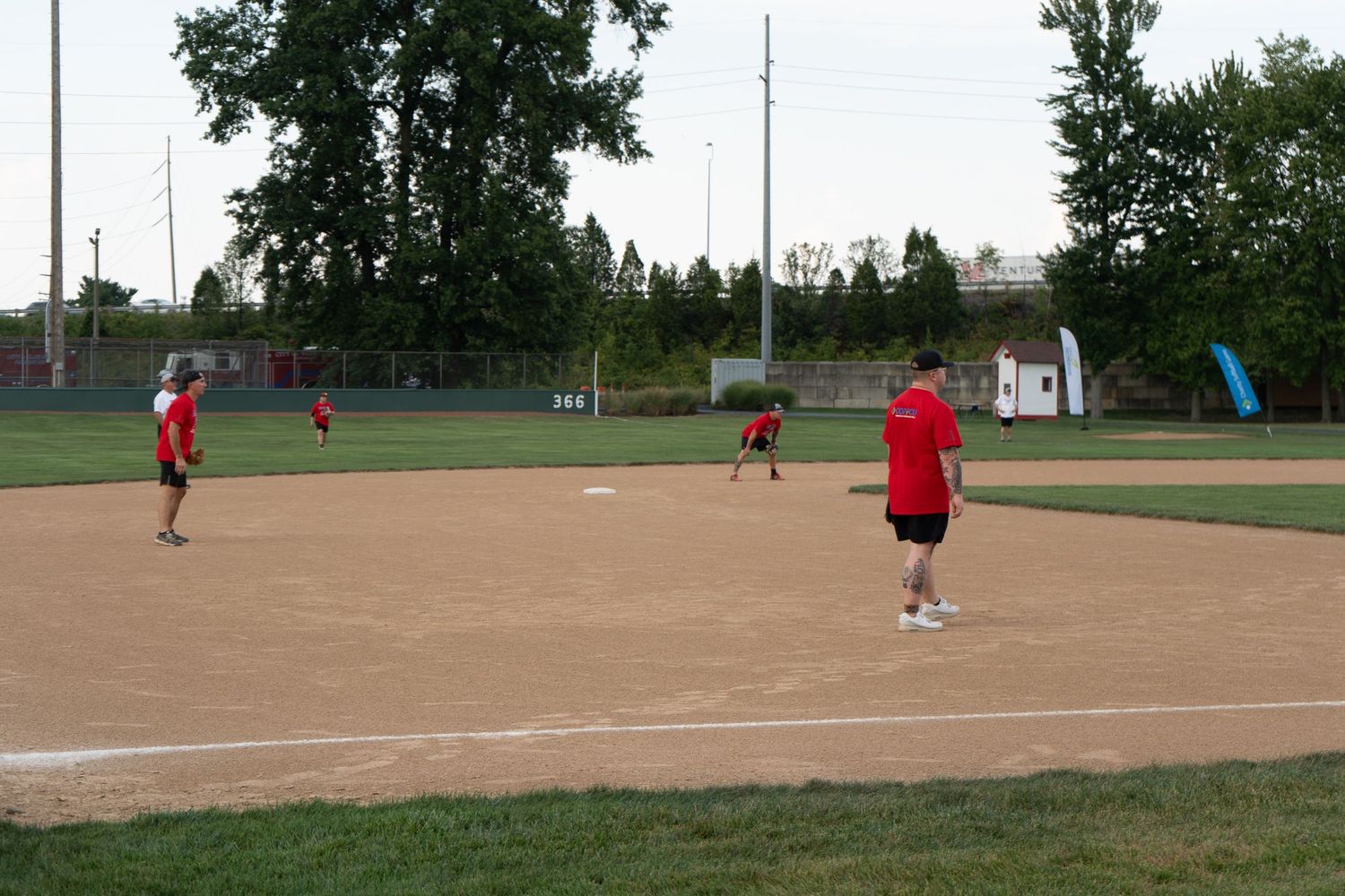 Red-shirted players practice fielding positions on a well-maintained softball diamond at dusk.