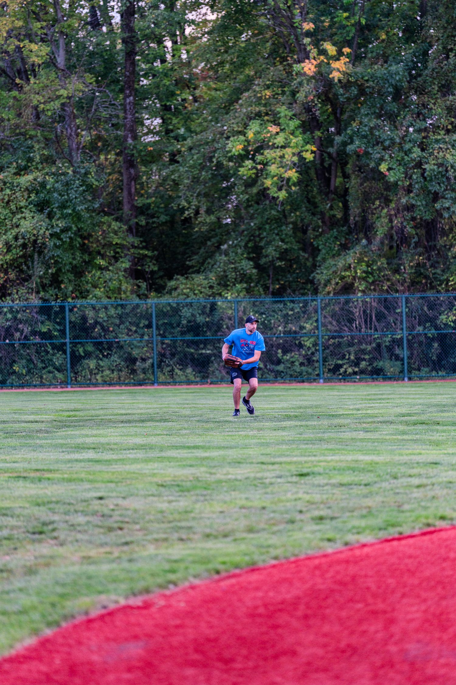 Male outfielder in blue jersey running across green grass field during baseball game near tree line.