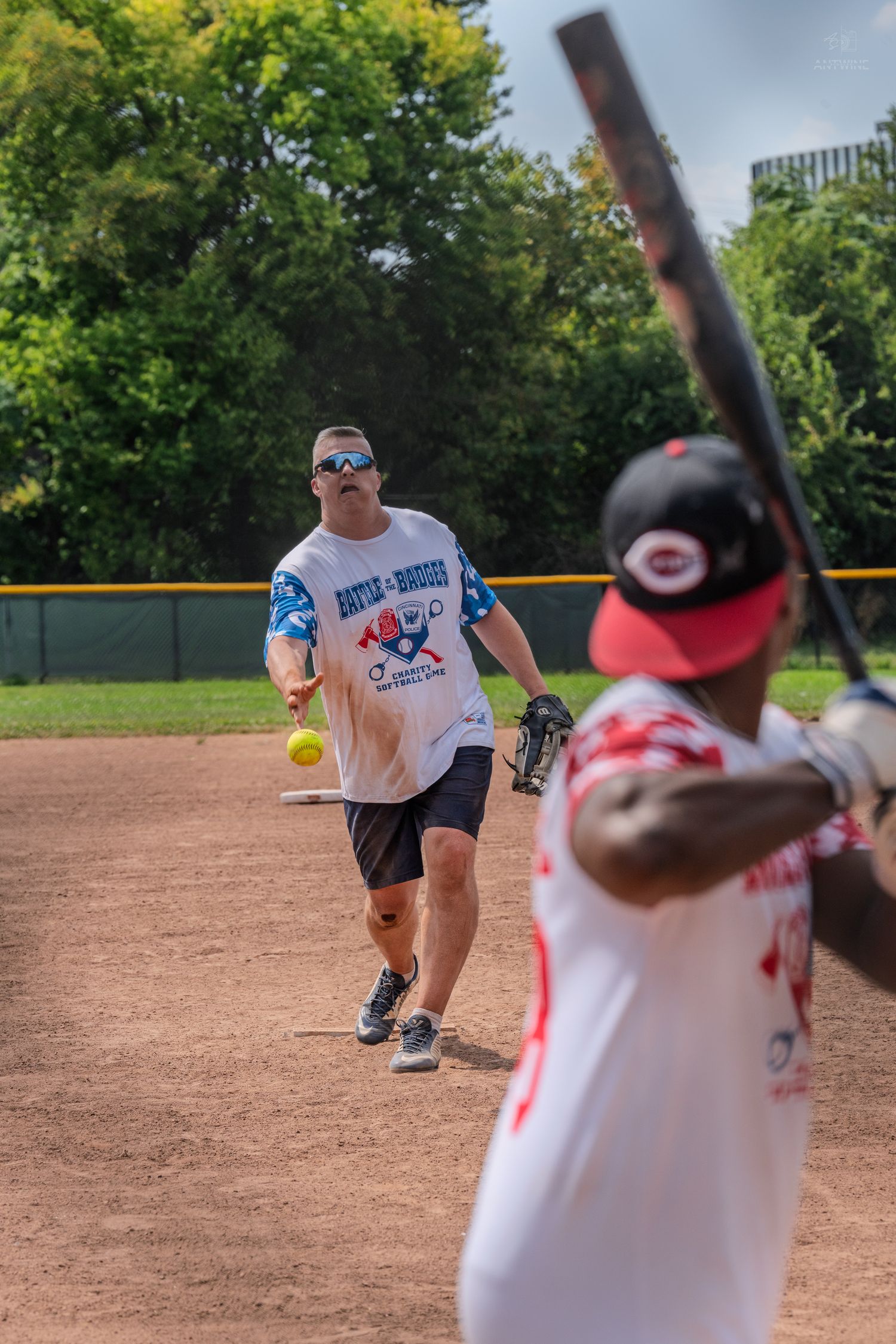 A pitcher throws a yellow softball toward a batter during an outdoor recreational softball game on a dirt field.