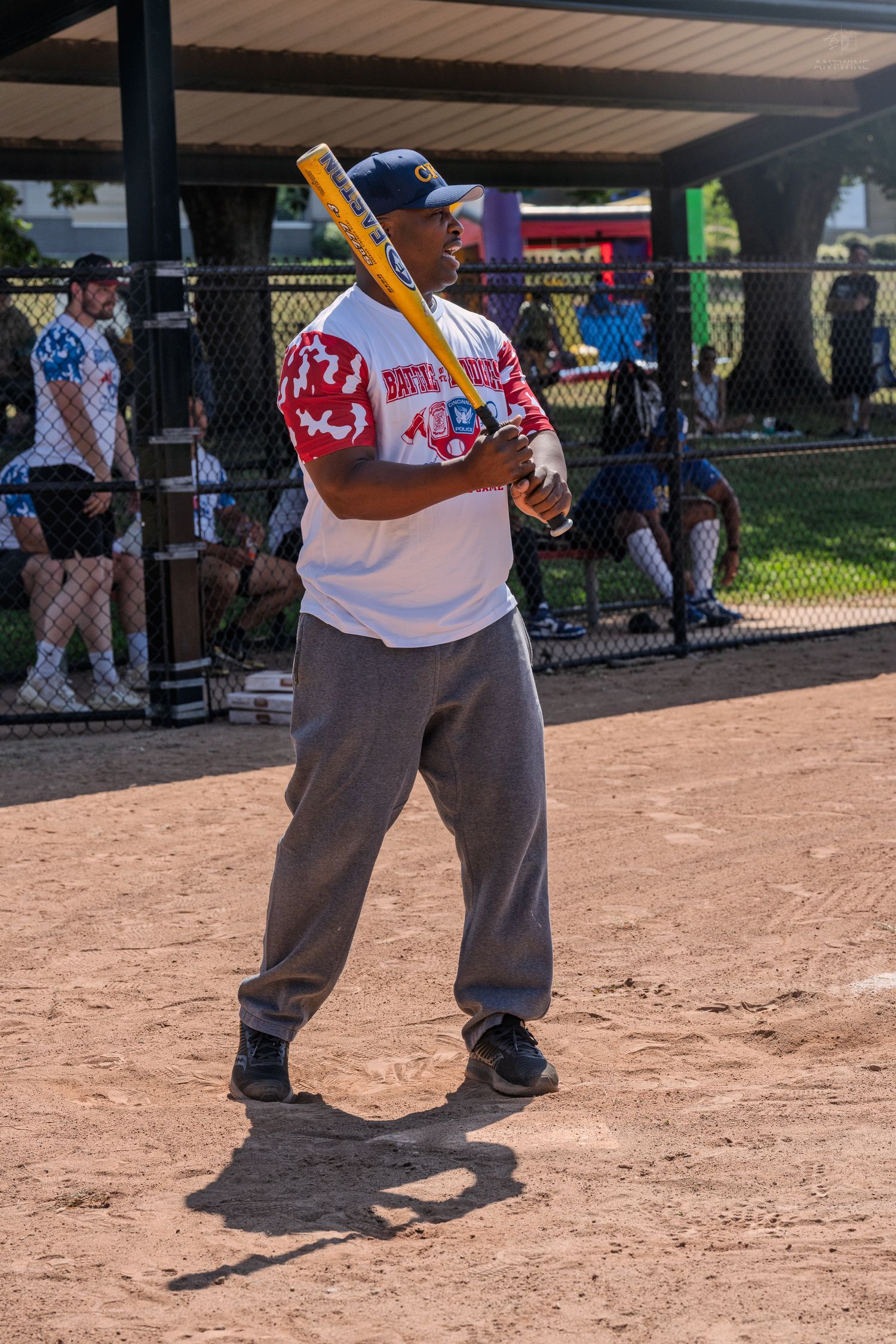 A baseball batter stands ready at home plate holding a yellow bat during an outdoor softball game.