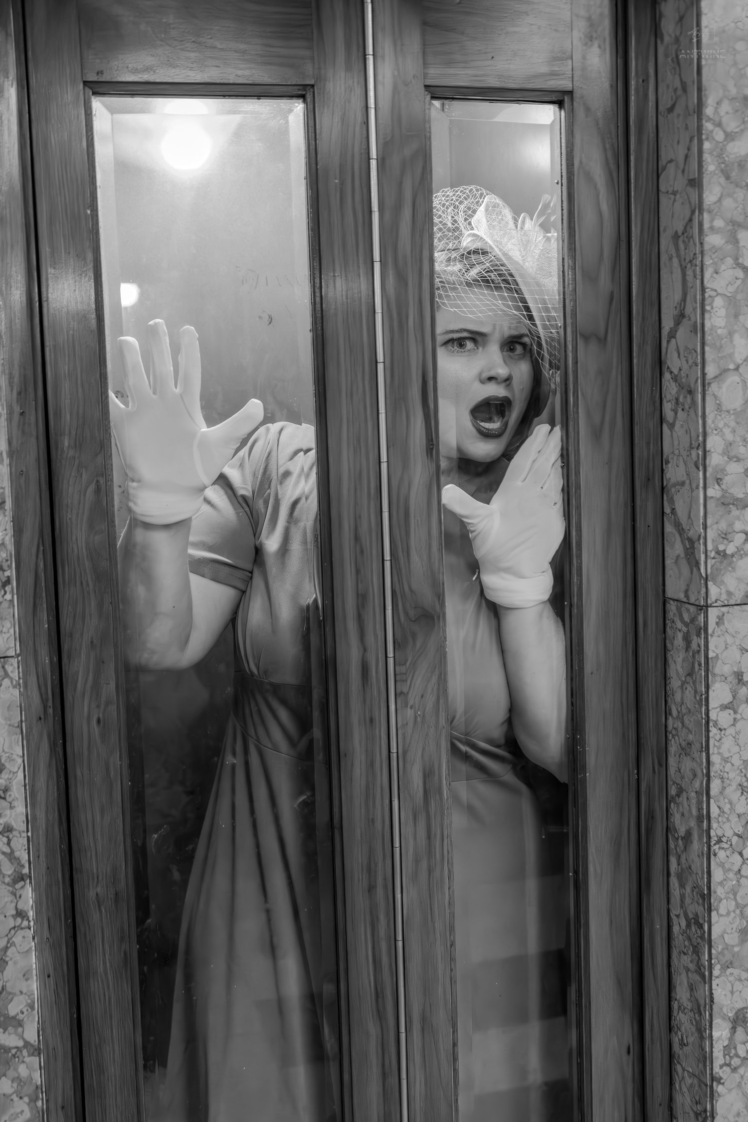 Black and white photo of a frightened woman in vintage hat and gloves pressing against glass doors, screaming.