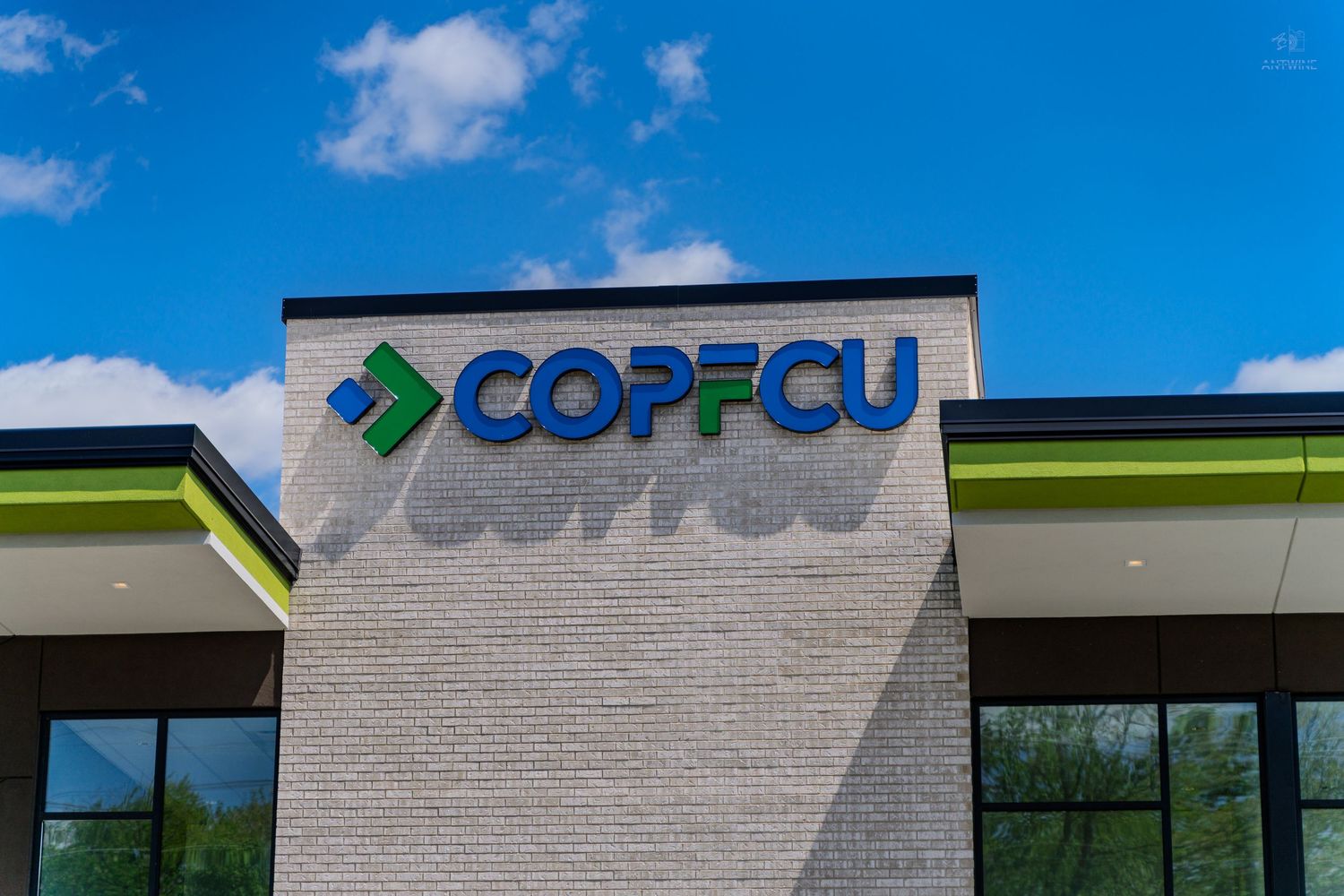 COPFCU credit union modern brick building exterior with green and blue logo signage against a blue sky.