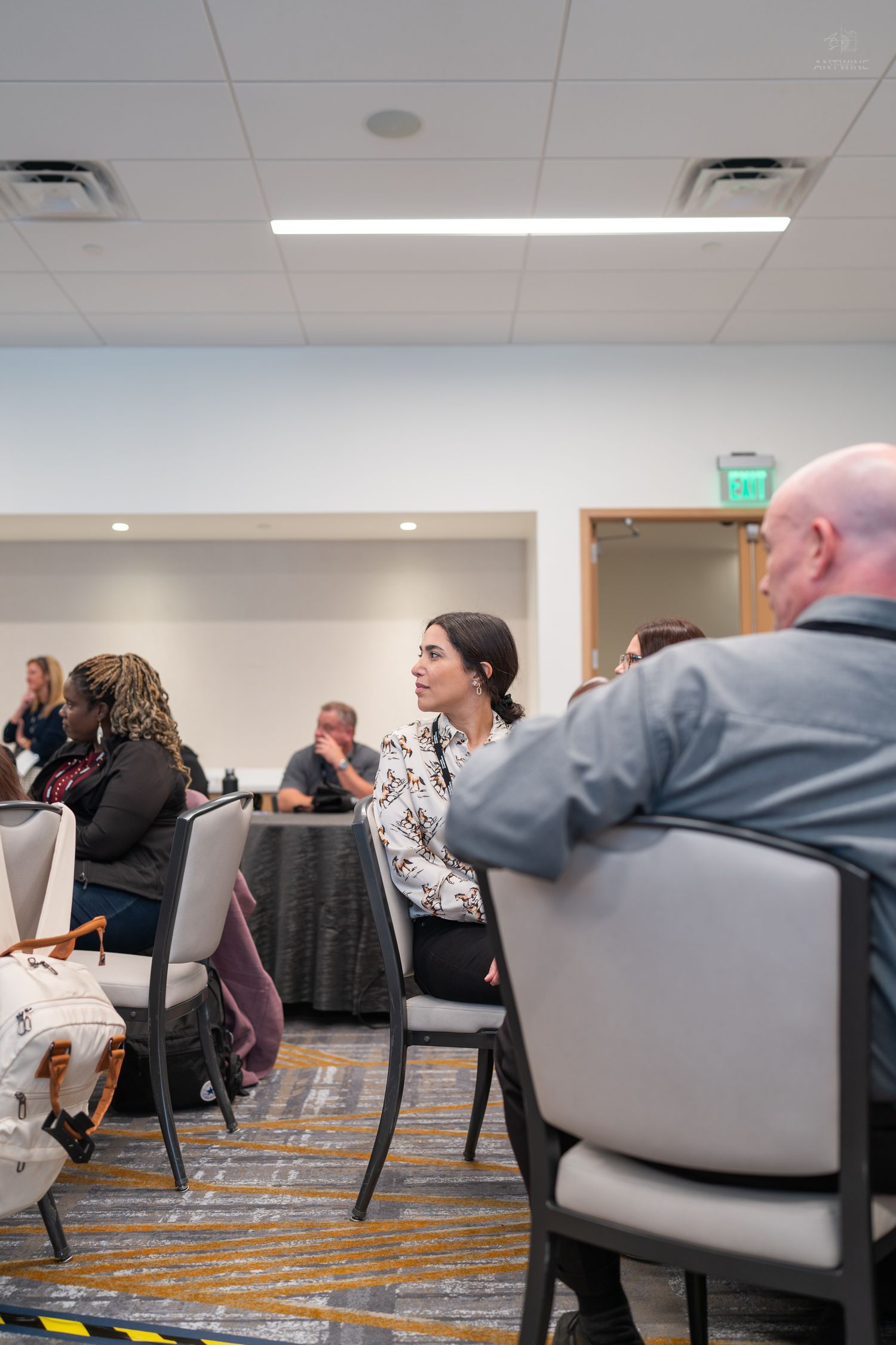 Professional woman in floral blouse attends a conference session, seated among other attendees in a meeting room.
