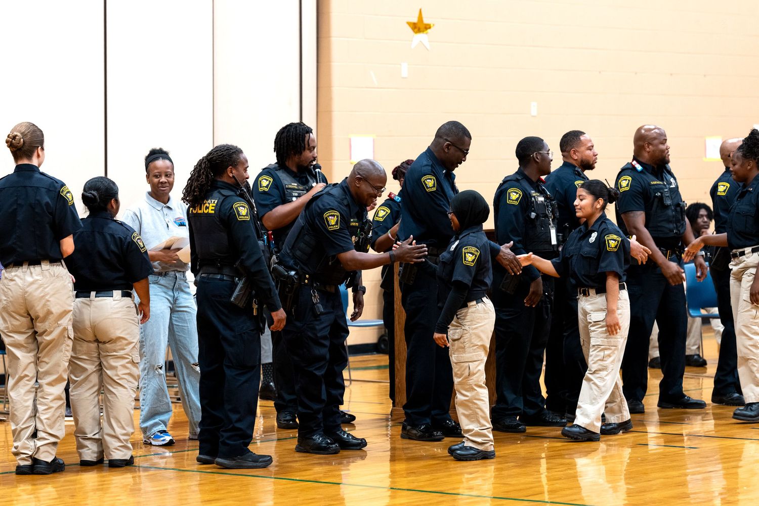 Law enforcement officers in uniform interact with students in a school gymnasium during a community outreach event.