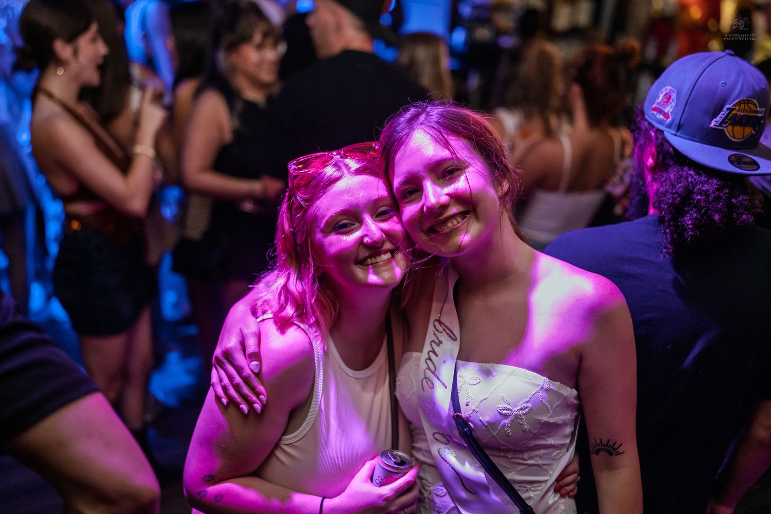 Two happy women hugging under pink neon lights at a vibrant nightclub.