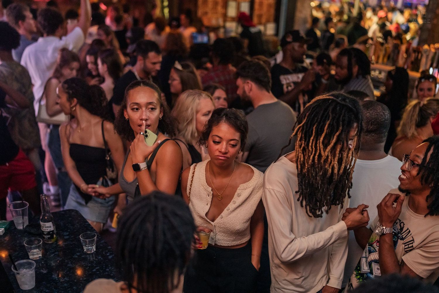 Young adults socializing and dancing in a crowded nightclub with warm ambient lighting.