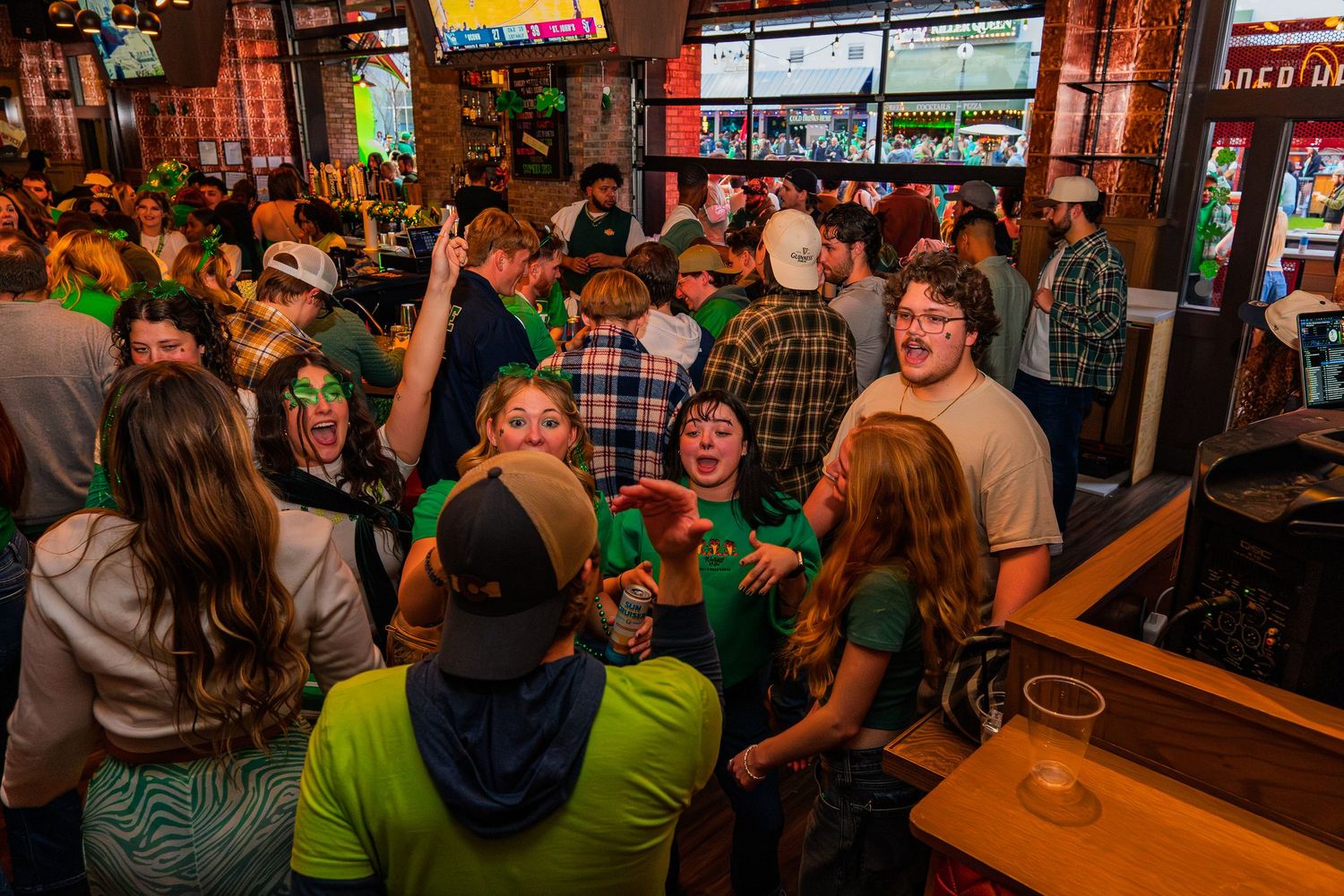 Packed sports bar filled with St. Patrick's Day revelers dressed in green celebrating together.