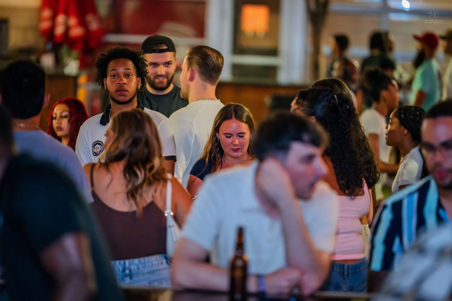 Diverse group of young adults mingling in a lively crowded bar with warm lighting.