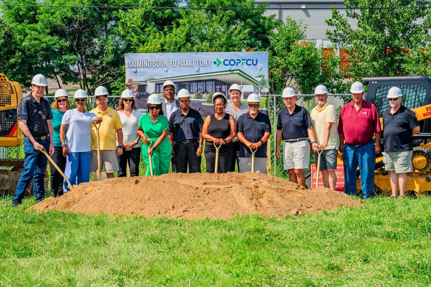 Large group in hard hats holding golden shovels at COPCU Hamilton groundbreaking ceremony on sunny day.