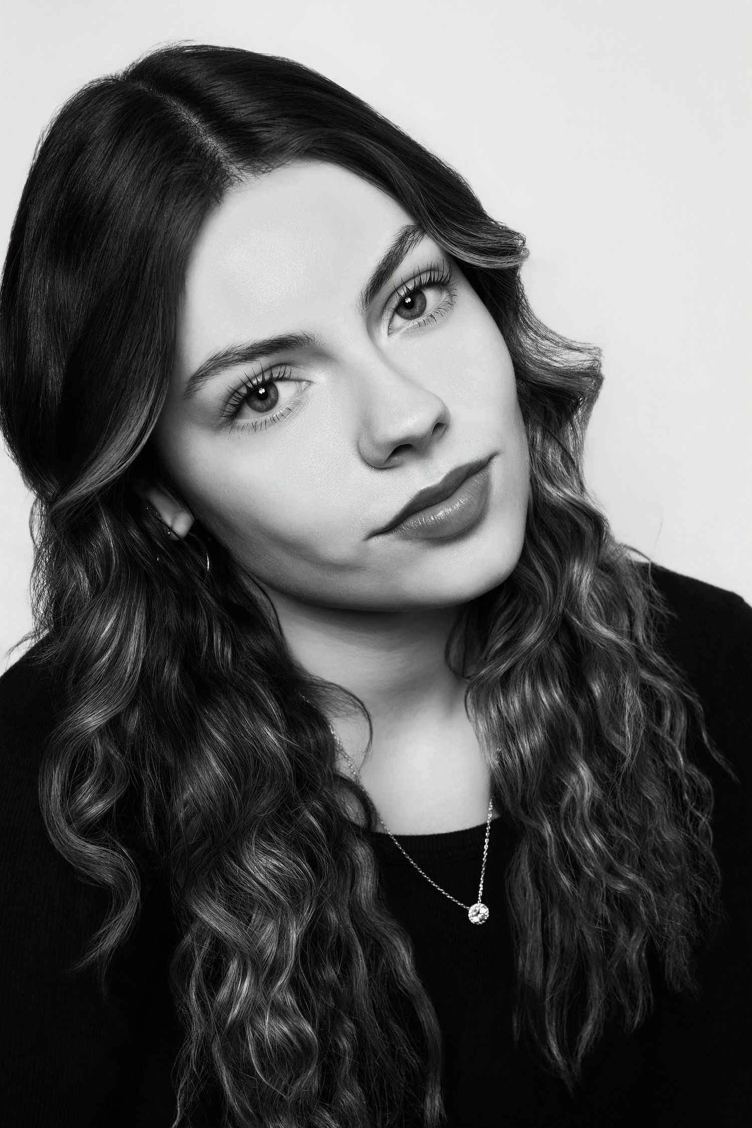 Black and white close-up portrait of a young woman with wavy hair and a small pendant necklace.