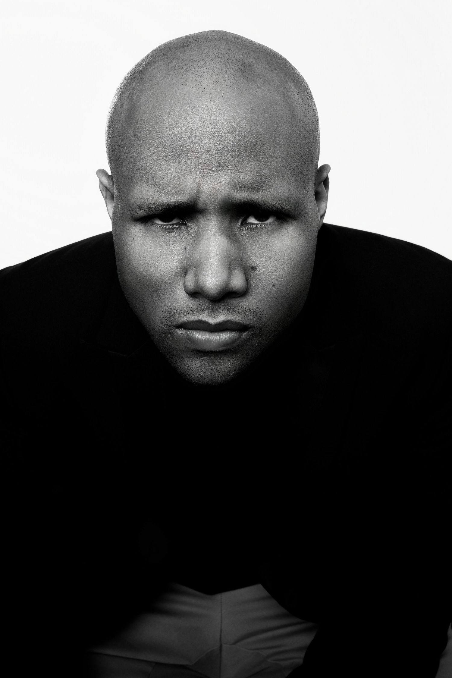 Bald Black man with furrowed brow and serious expression in black and white close-up portrait.