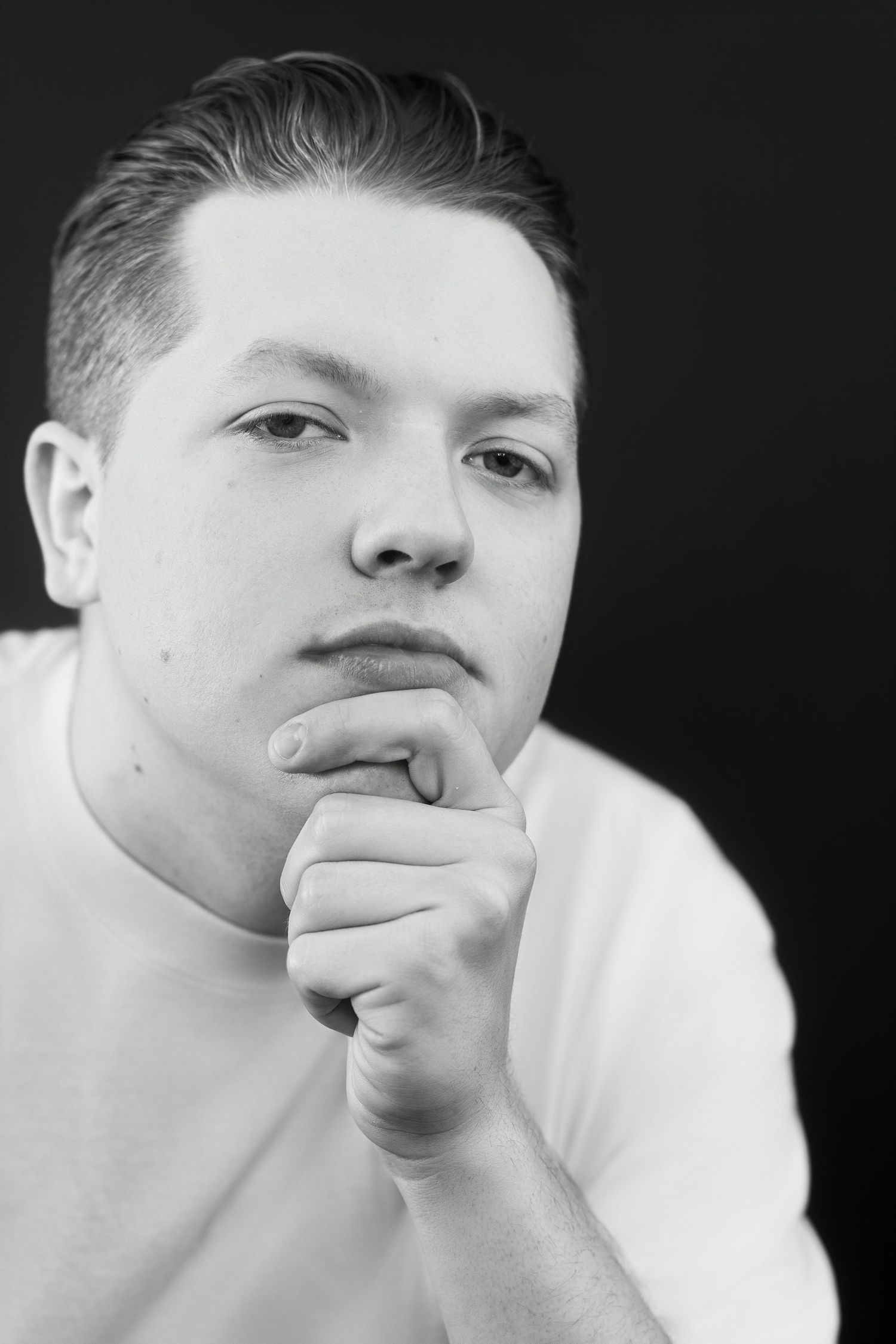 Black and white close-up portrait of young man resting chin on fist, pensive look.