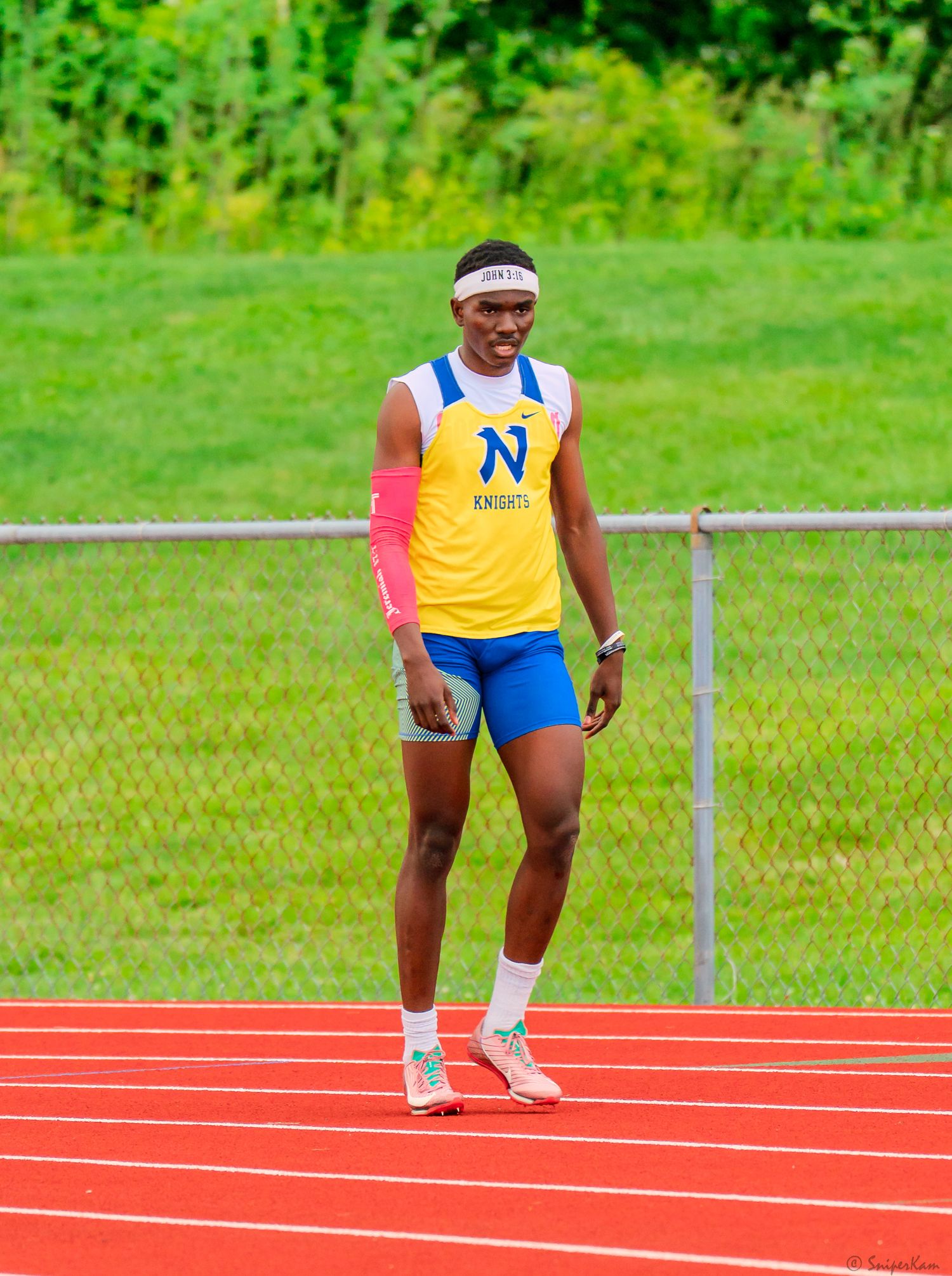 Male track athlete in yellow Knights uniform stands on red track at outdoor field event.