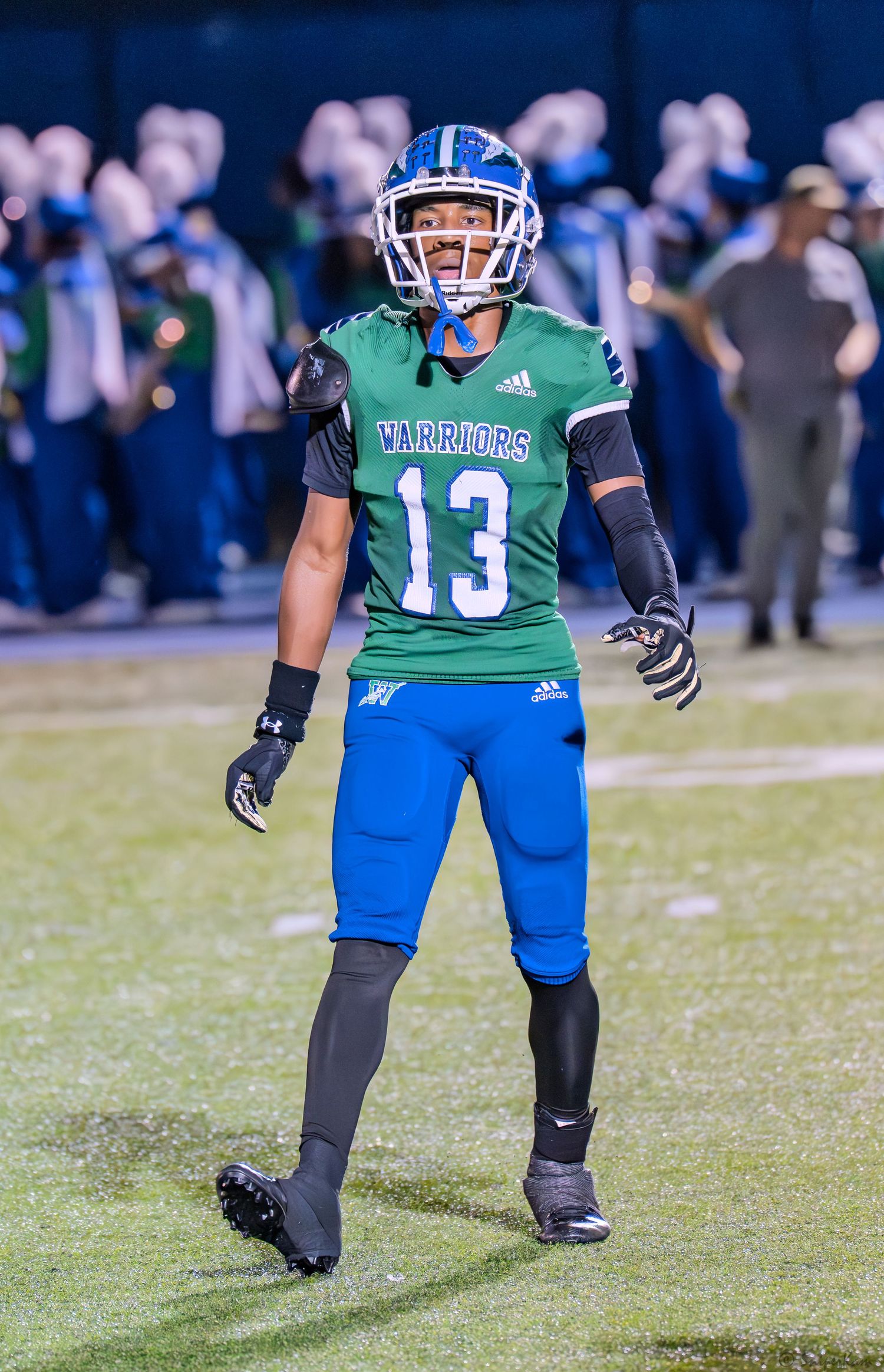 Warriors football player number 13 in green and blue uniform celebrates on the field during a night game.