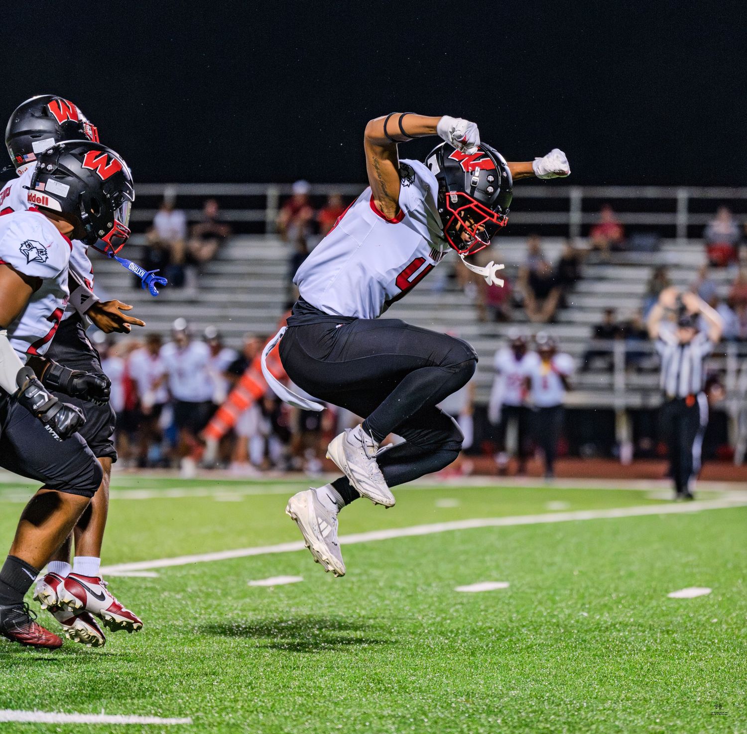 Colerain Cardinals football player leaps through the air during a night game.
