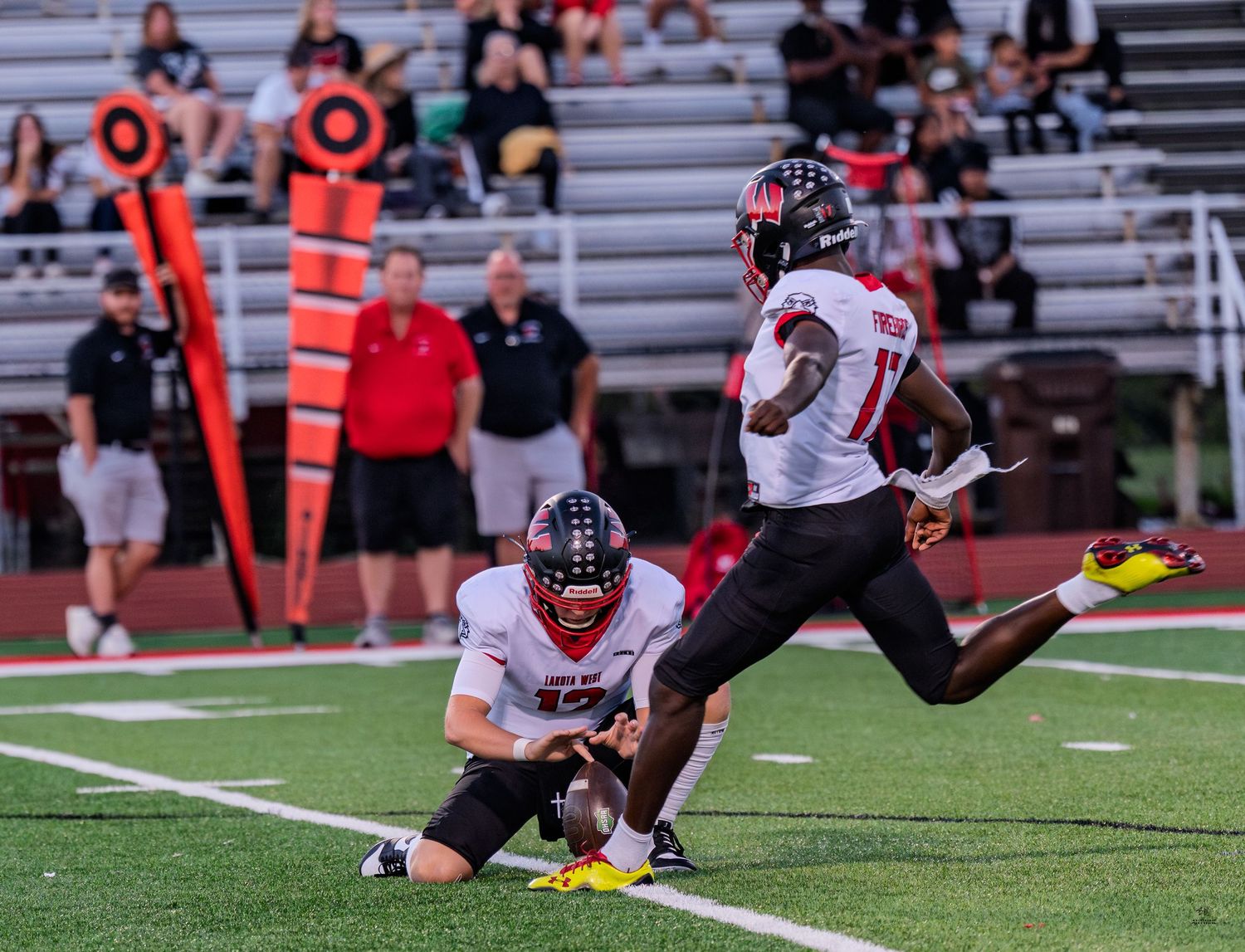 A football player leaps into the air after a kick during a nighttime high school football game.