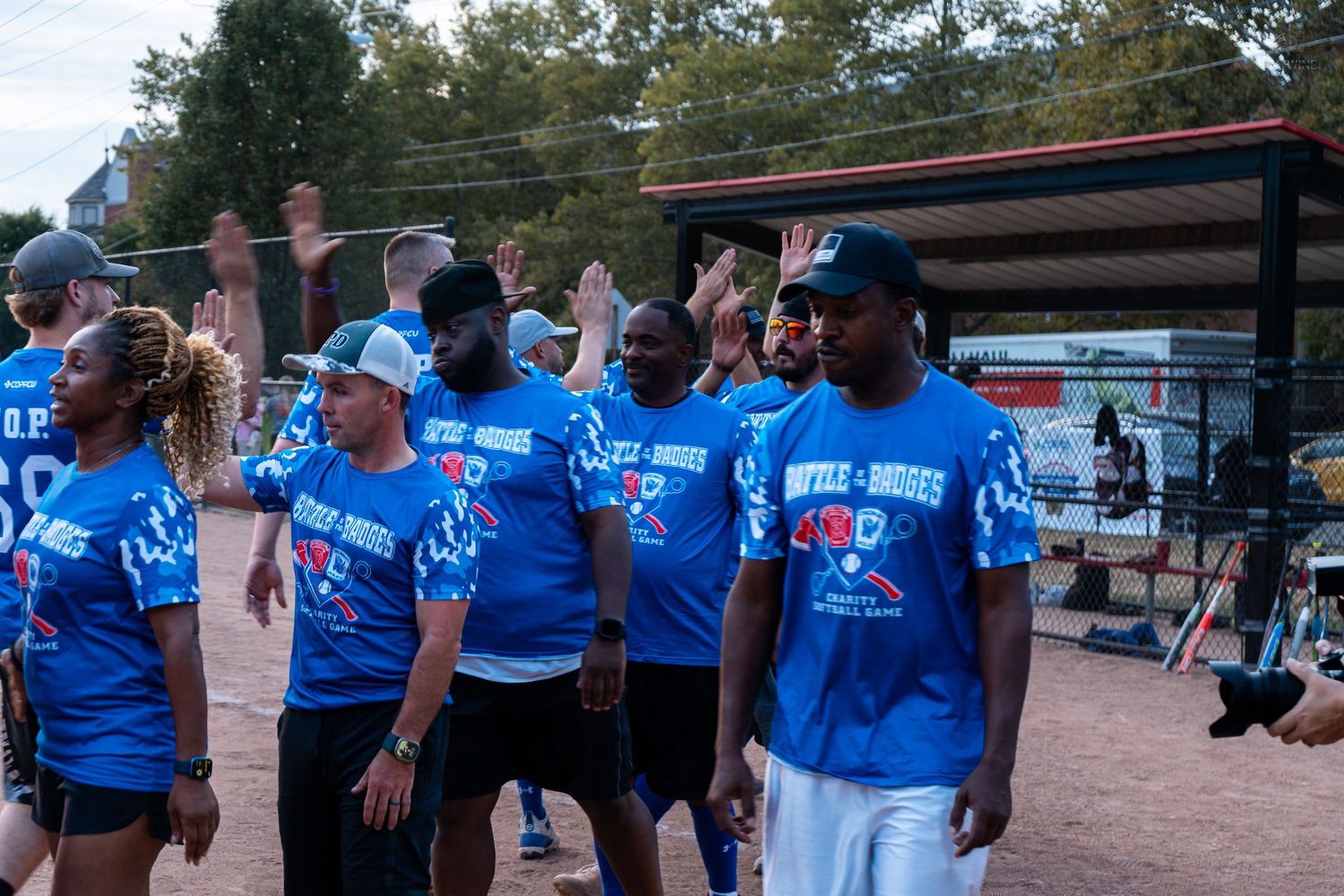 Blue team members in matching shirts walk together at an outdoor softball game event.