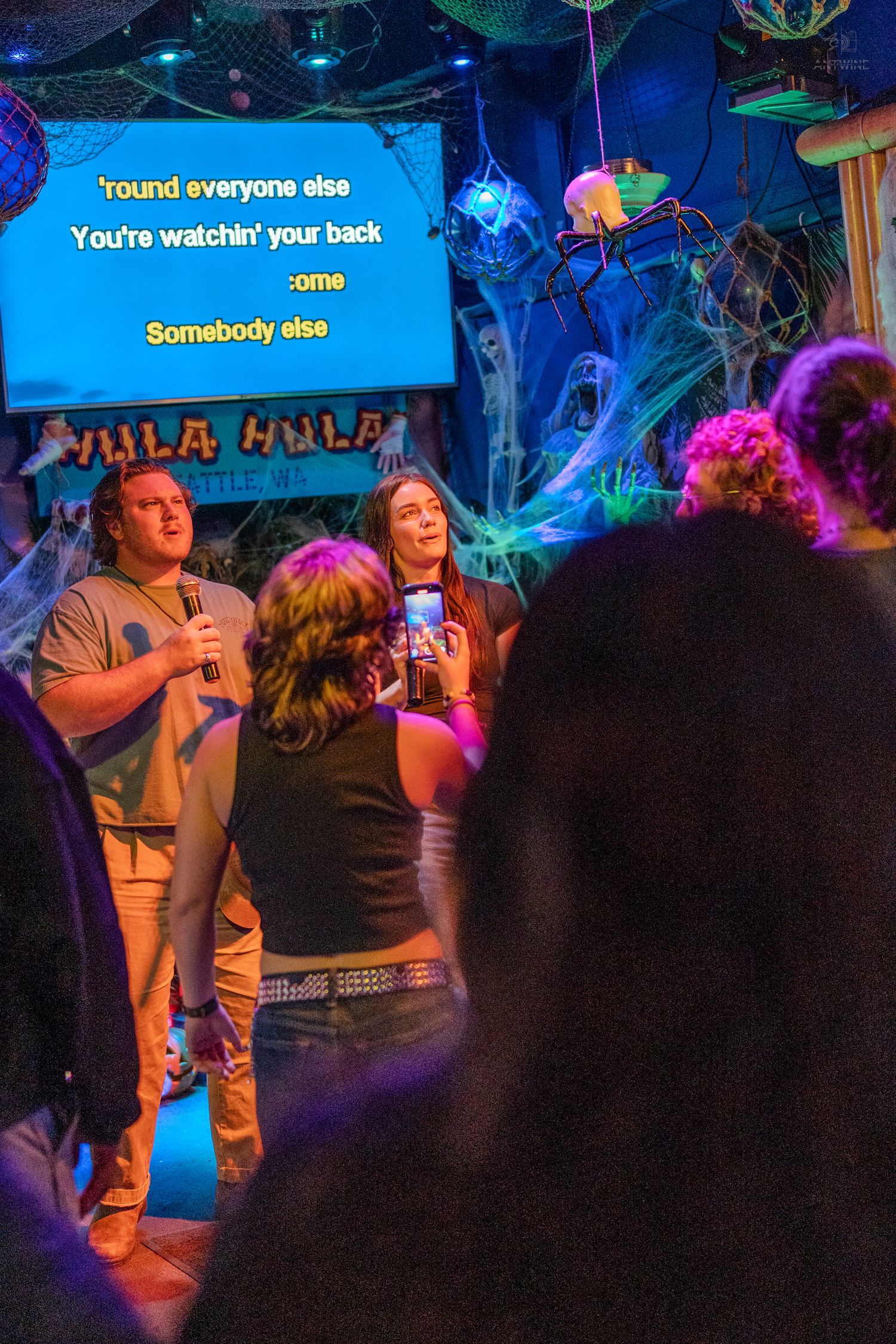 Man and woman singing karaoke duet at spooky Halloween-decorated Hula Hula bar in Seattle.