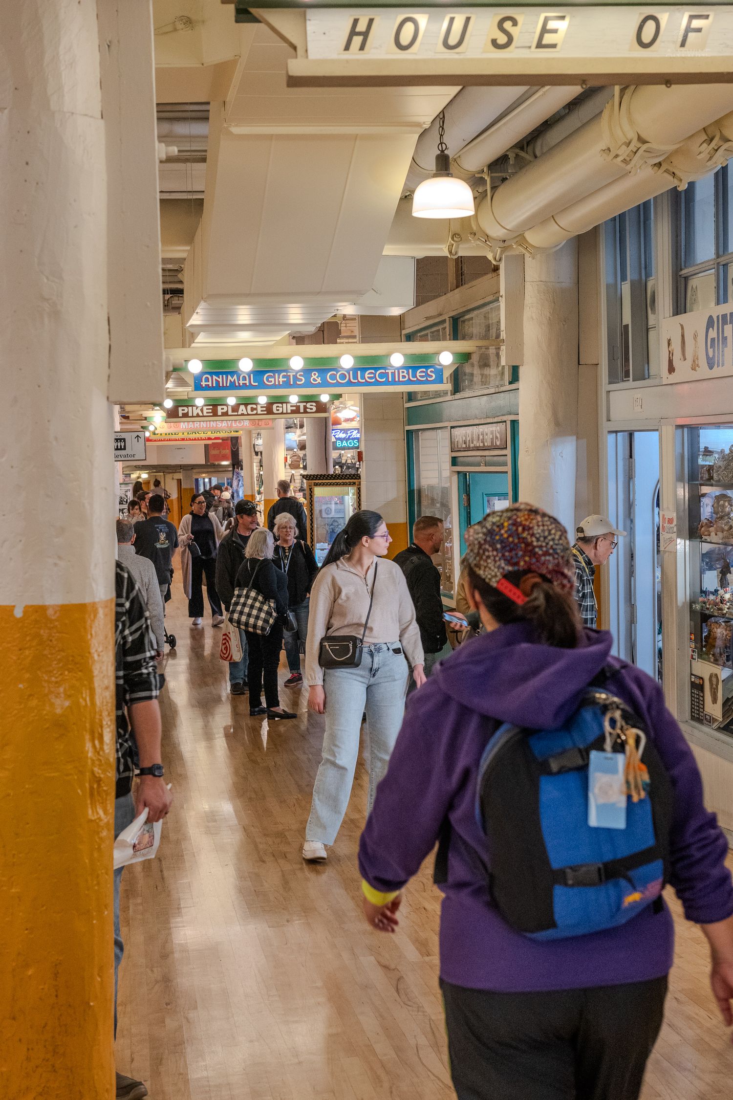 Busy indoor market hallway with shoppers passing gift and collectible stores under a House Of sign.